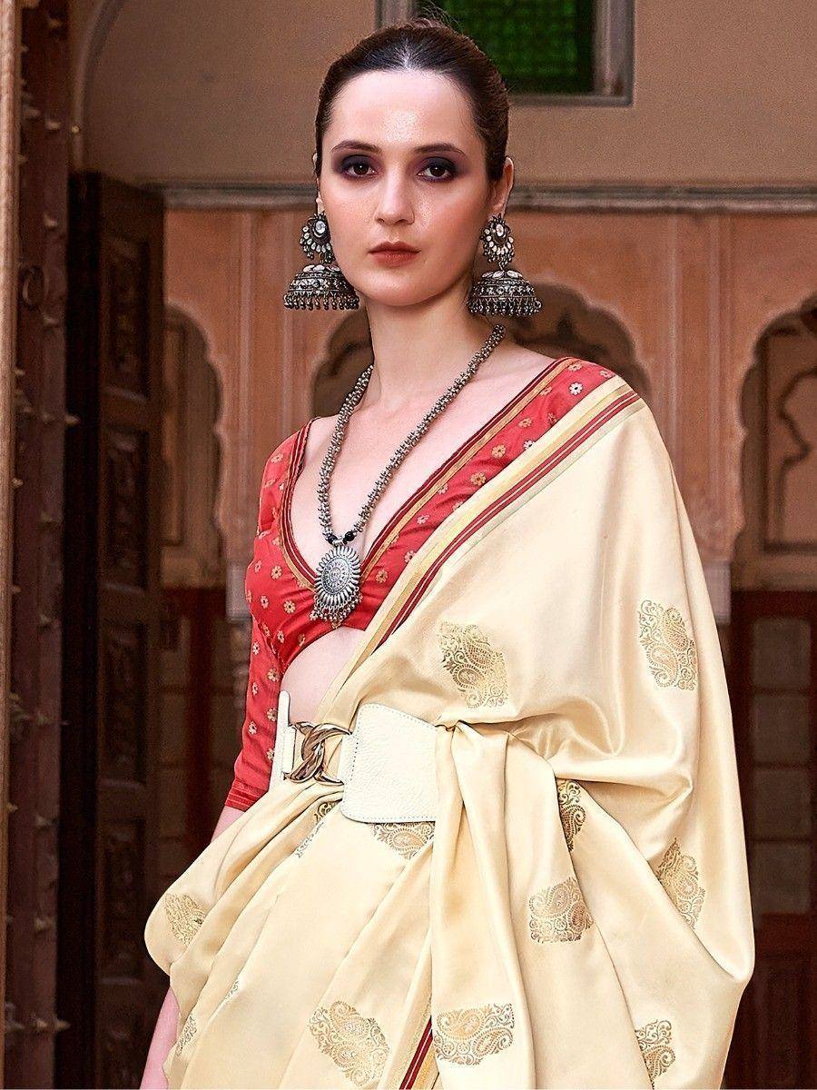Elegant cream saree with gold paisley print, paired with red blouse and statement jewelry, perfect for Indian ethnic occasions.