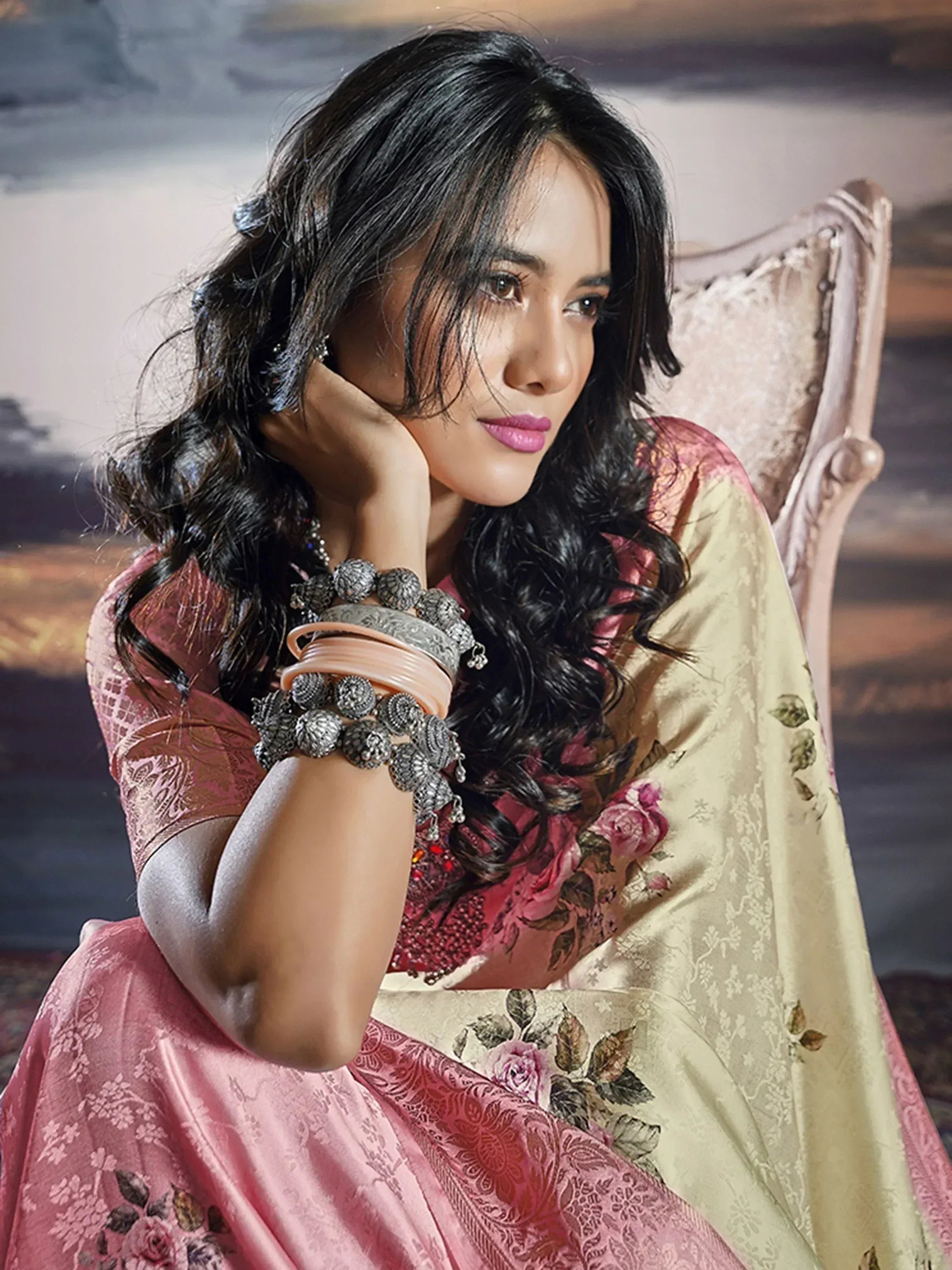 Woman in elegant pink floral saree with gold border, styled with silver bangles and traditional jewelry