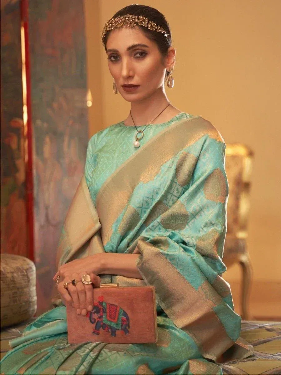 Woman in turquoise ethnic saree with gold border, holding elephant clutch, styled with maang tikka and pearl jewelry