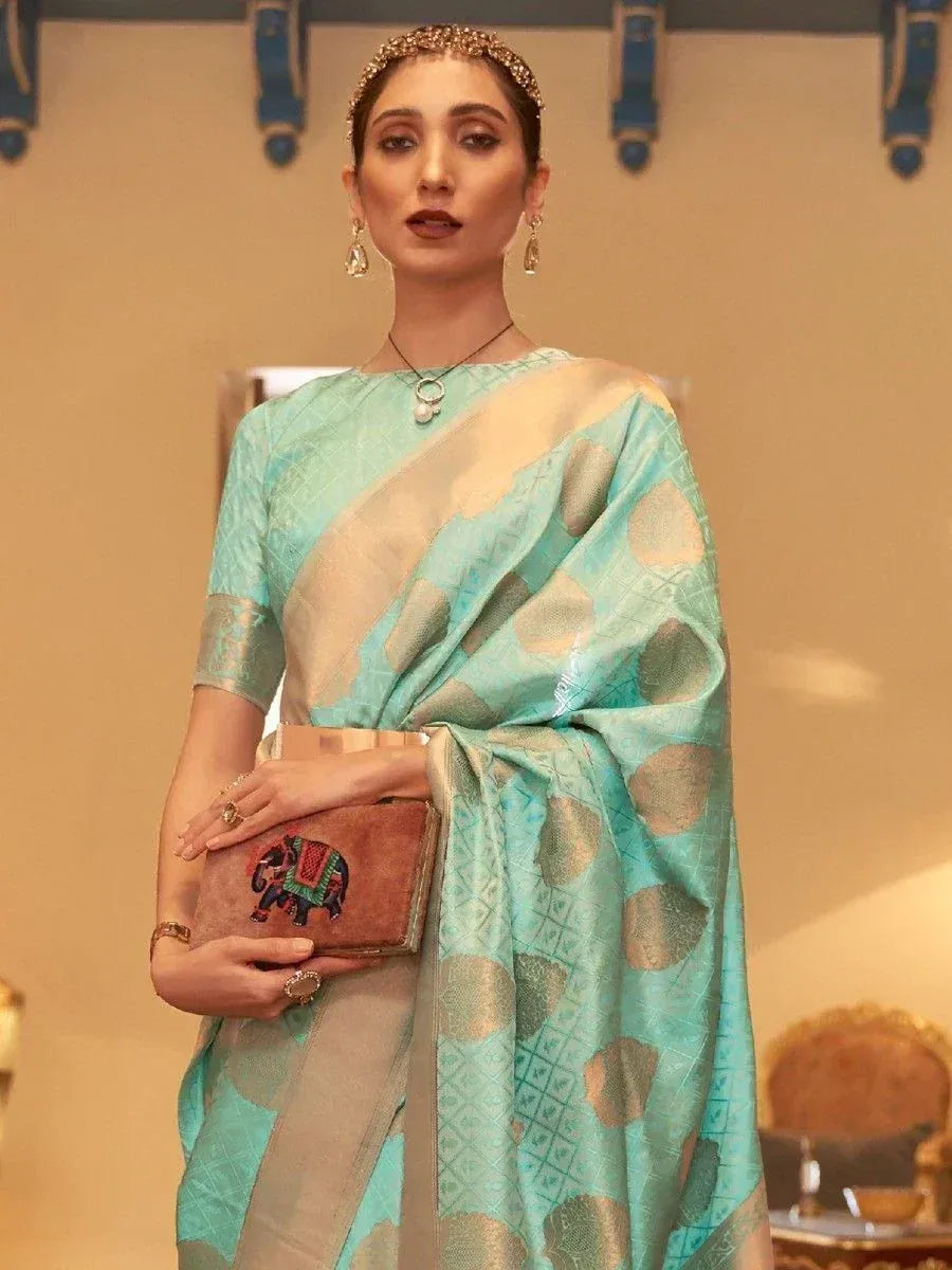 Woman in mint green designer saree with gold motifs, holding elephant clutch, traditional Indian ethnic wear