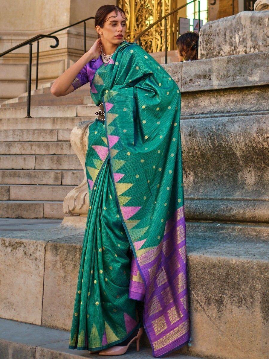 Emerald green saree with pink and gold geometric patterns, paired with purple blouse, styled on stone steps