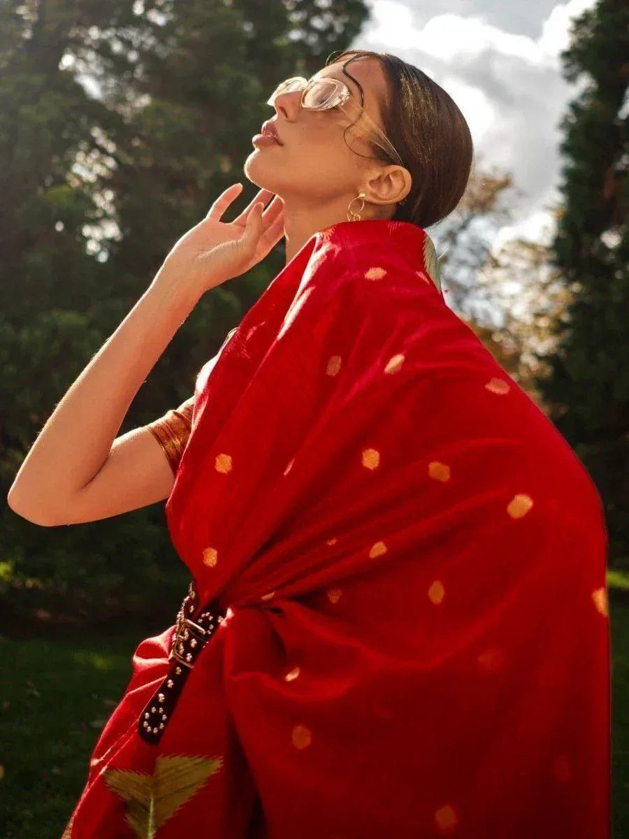 Woman in red ethnic saree with gold dots, styled with belt and sunglasses, outdoors