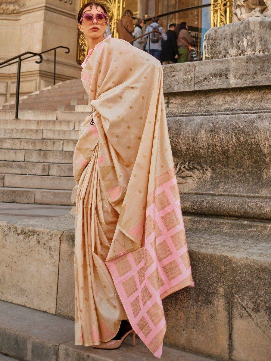 Beige and pink designer saree with gold polka dots and checkered border, styled on stone steps