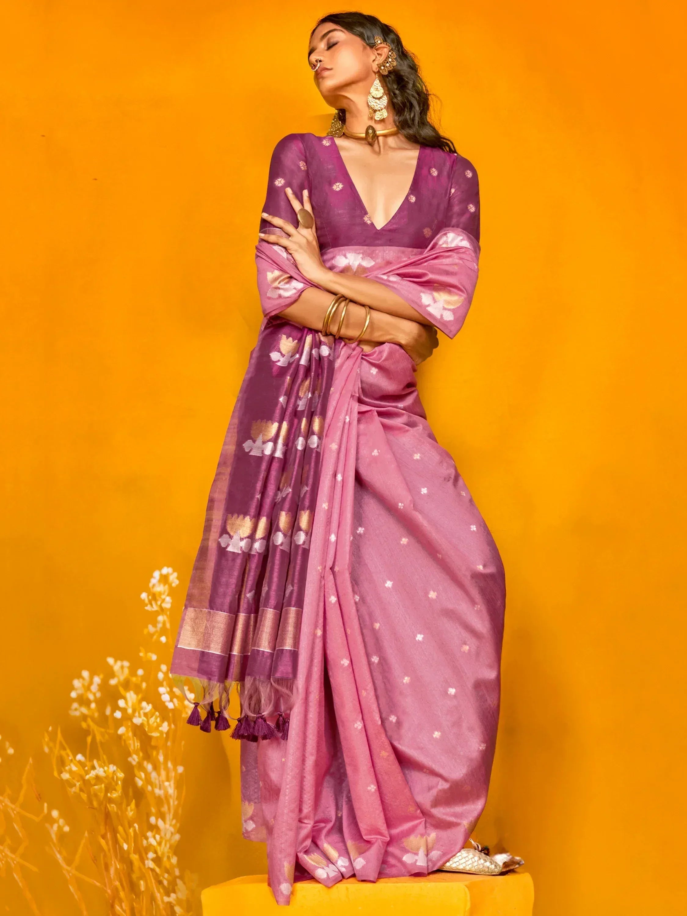 Woman in purple floral saree with gold jewelry against orange backdrop, ethnic Indian wear