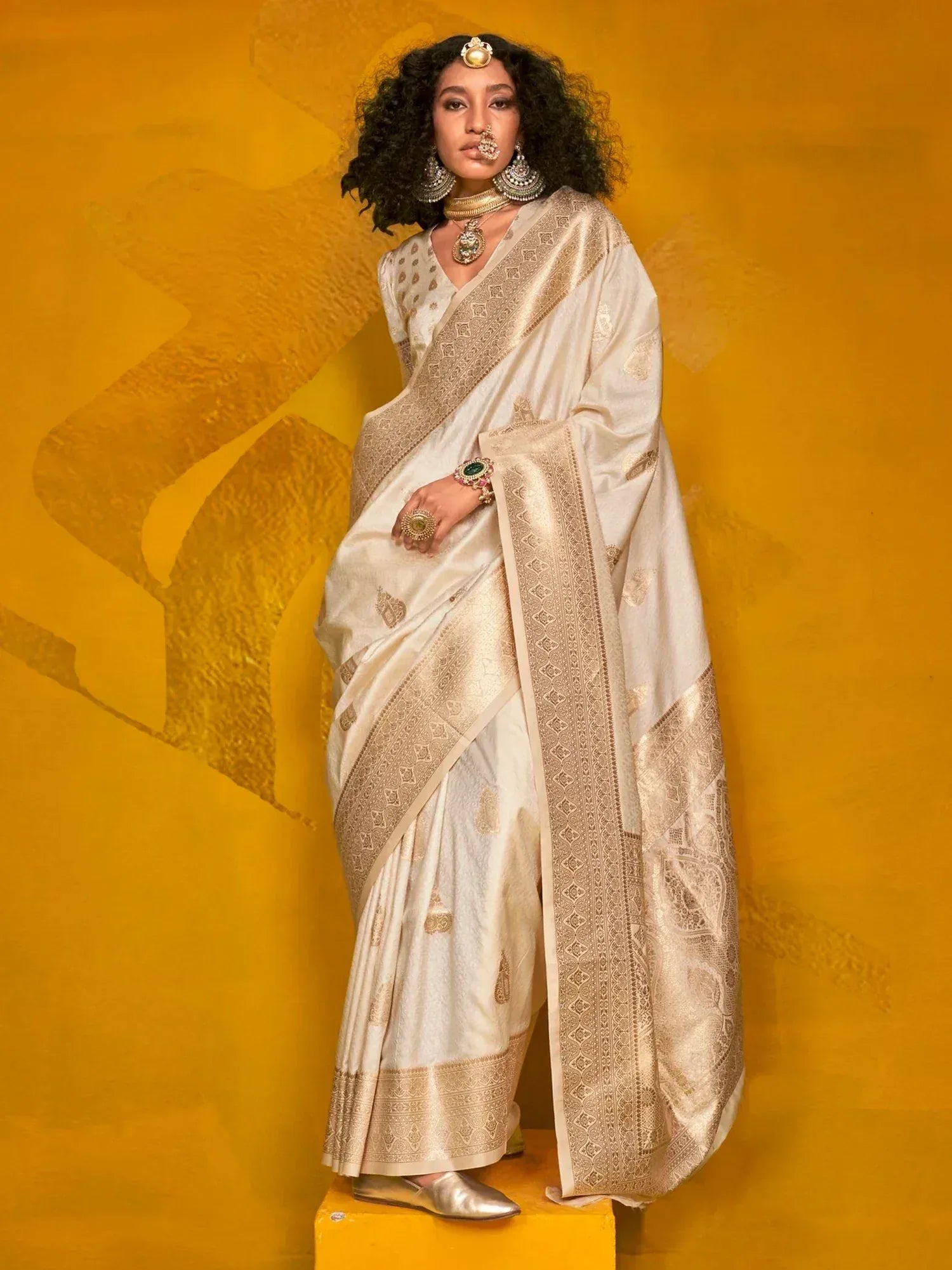 Elegant ivory saree with gold embroidery, styled with traditional jewelry against a mustard backdrop