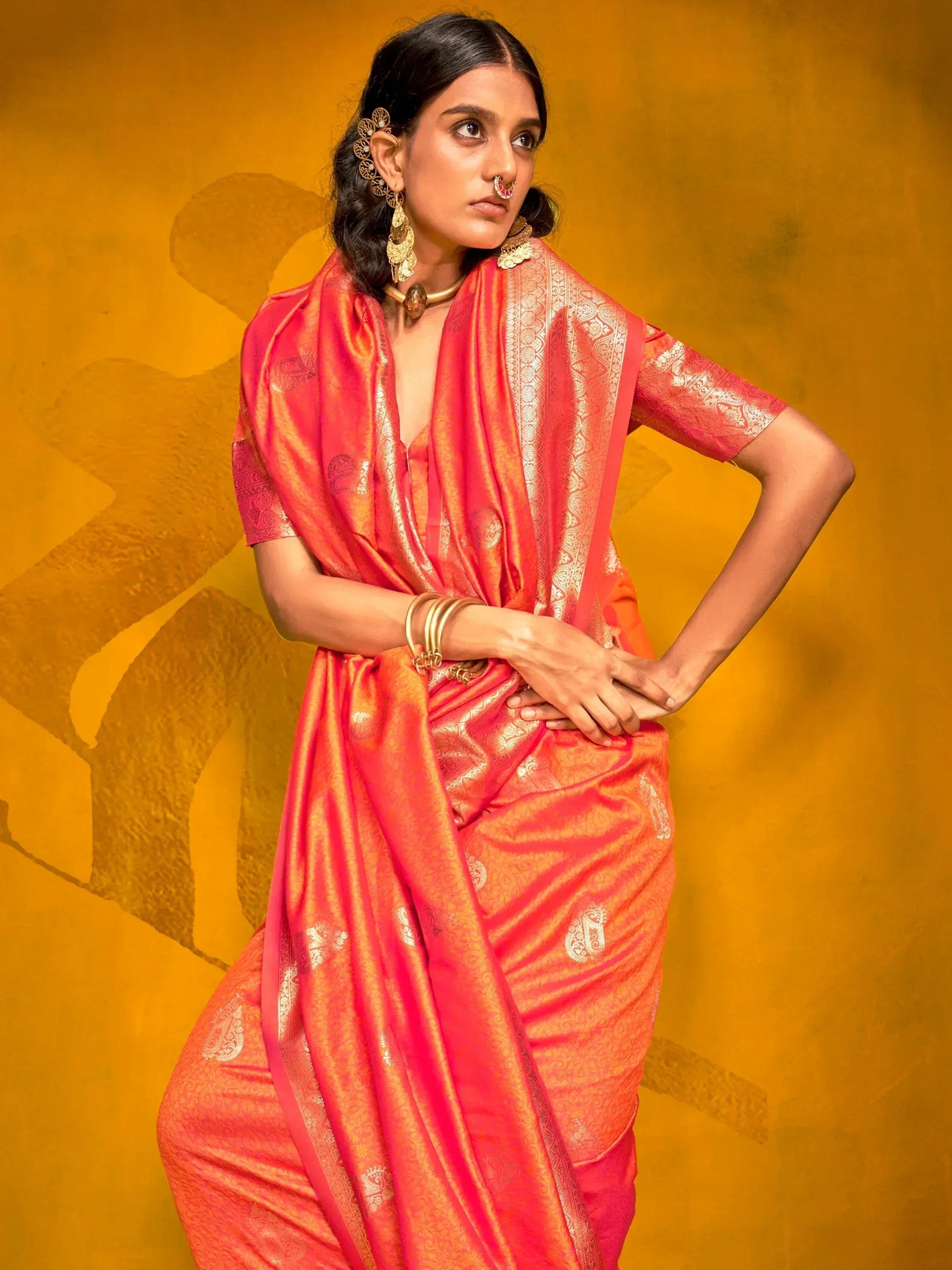 Woman in vibrant coral saree with gold paisley print, traditional Indian ethnic wear, styled with gold jewelry