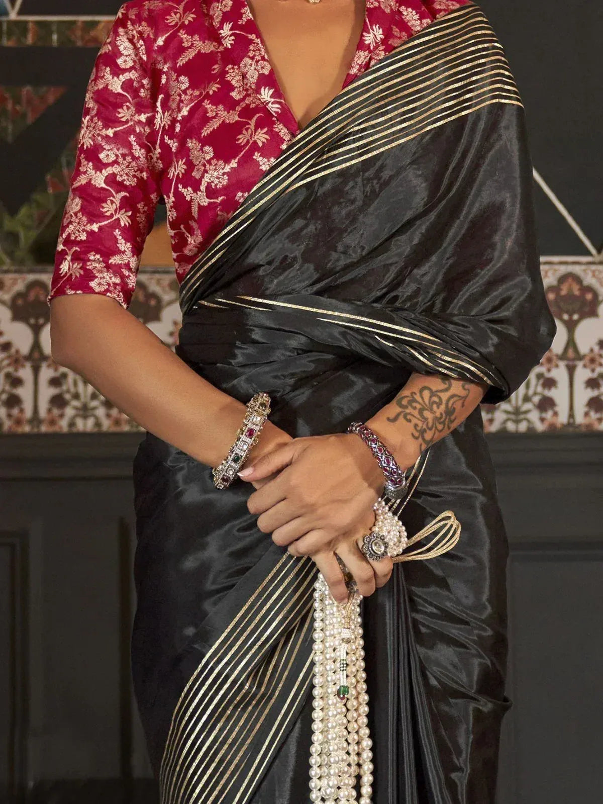 Black silk saree with gold stripes paired with red floral blouse, adorned with pearl jewelry and bangles