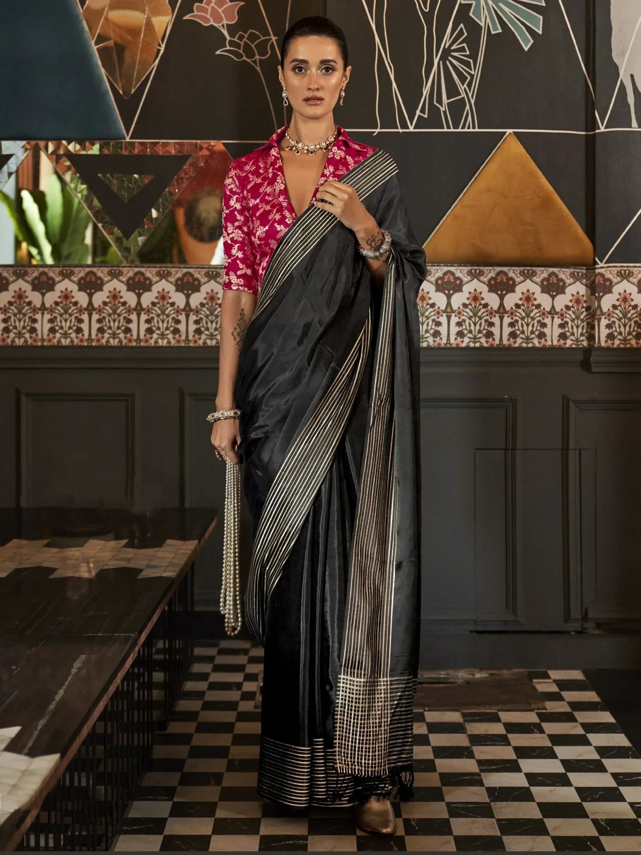 Elegant black saree with gold stripes paired with a pink floral blouse, styled for Indian ethnic wear.