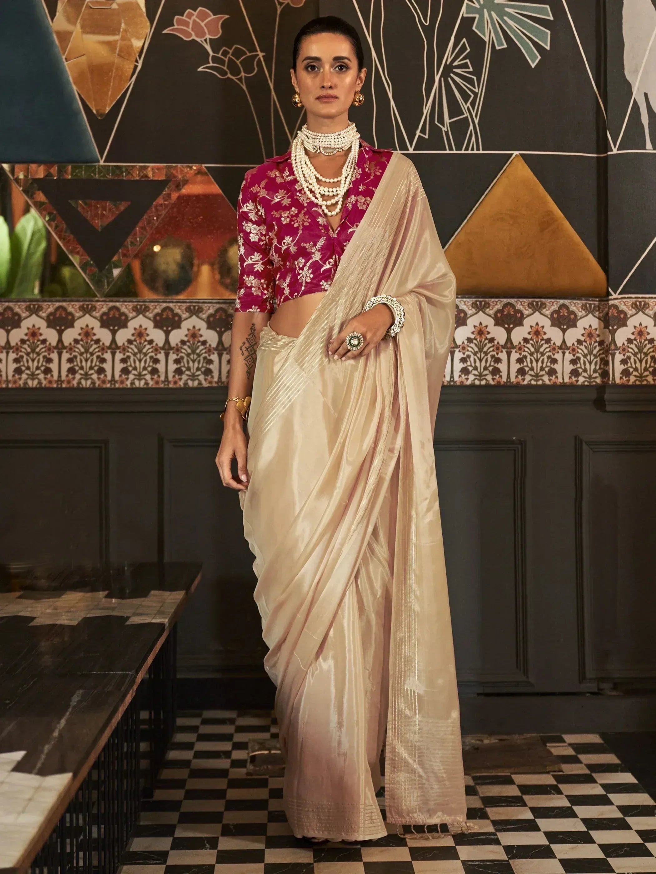 Elegant woman in cream silk saree with pink floral blouse, styled with pearl jewelry for Indian ethnic wear.