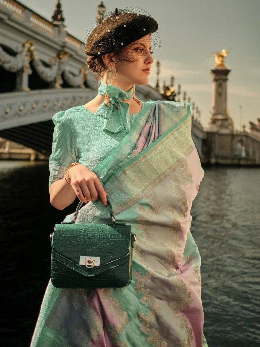 Woman in mint green designer saree with gold motifs, black beret, and green handbag near bridge