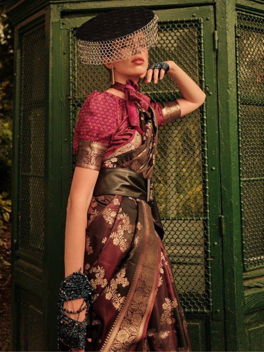 Elegant maroon and gold ethnic gown with intricate embroidery, styled with a black hat and beaded accessories