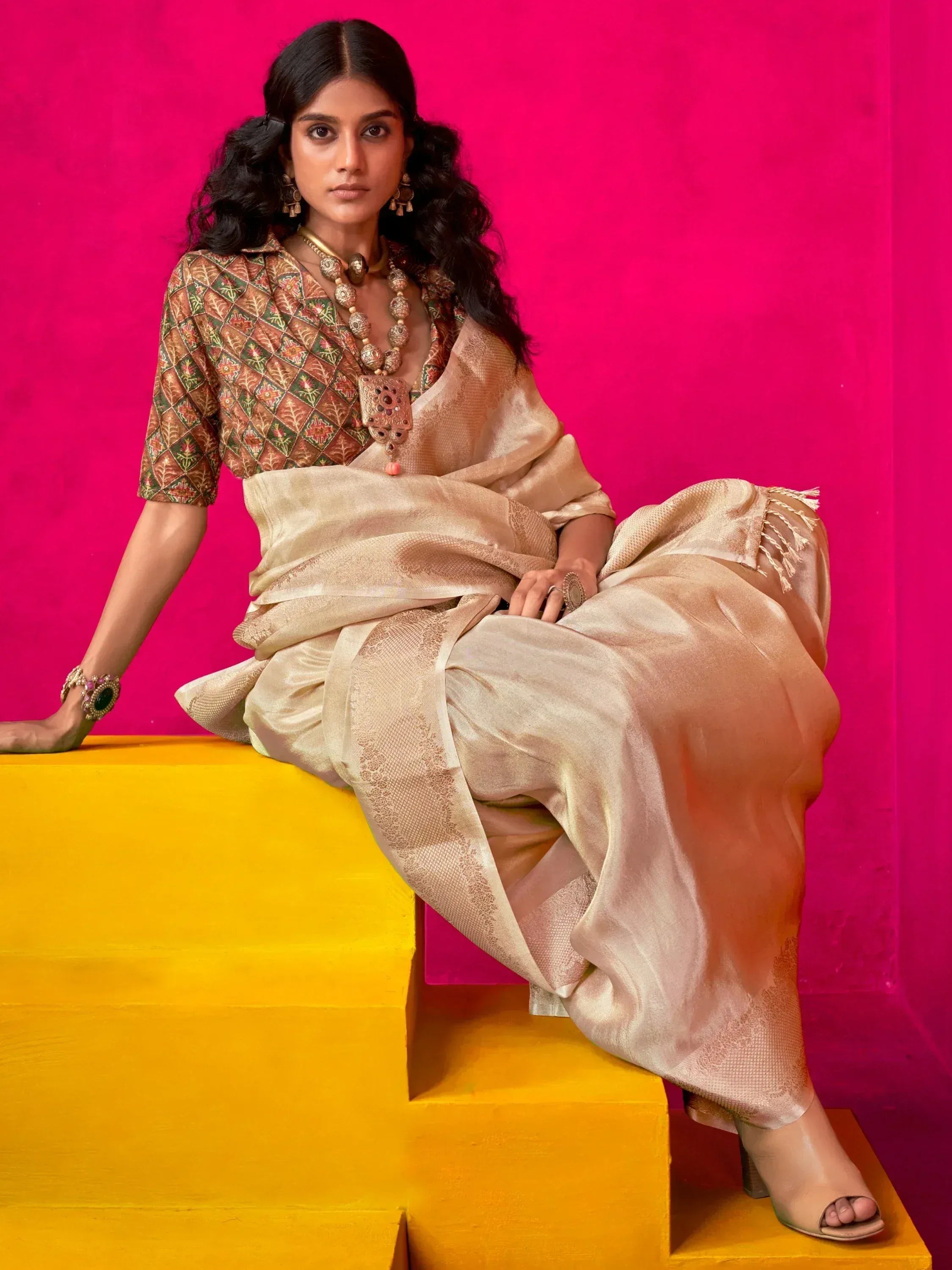 Elegant woman in designer saree with intricate blouse, traditional jewelry, and bold pink background
