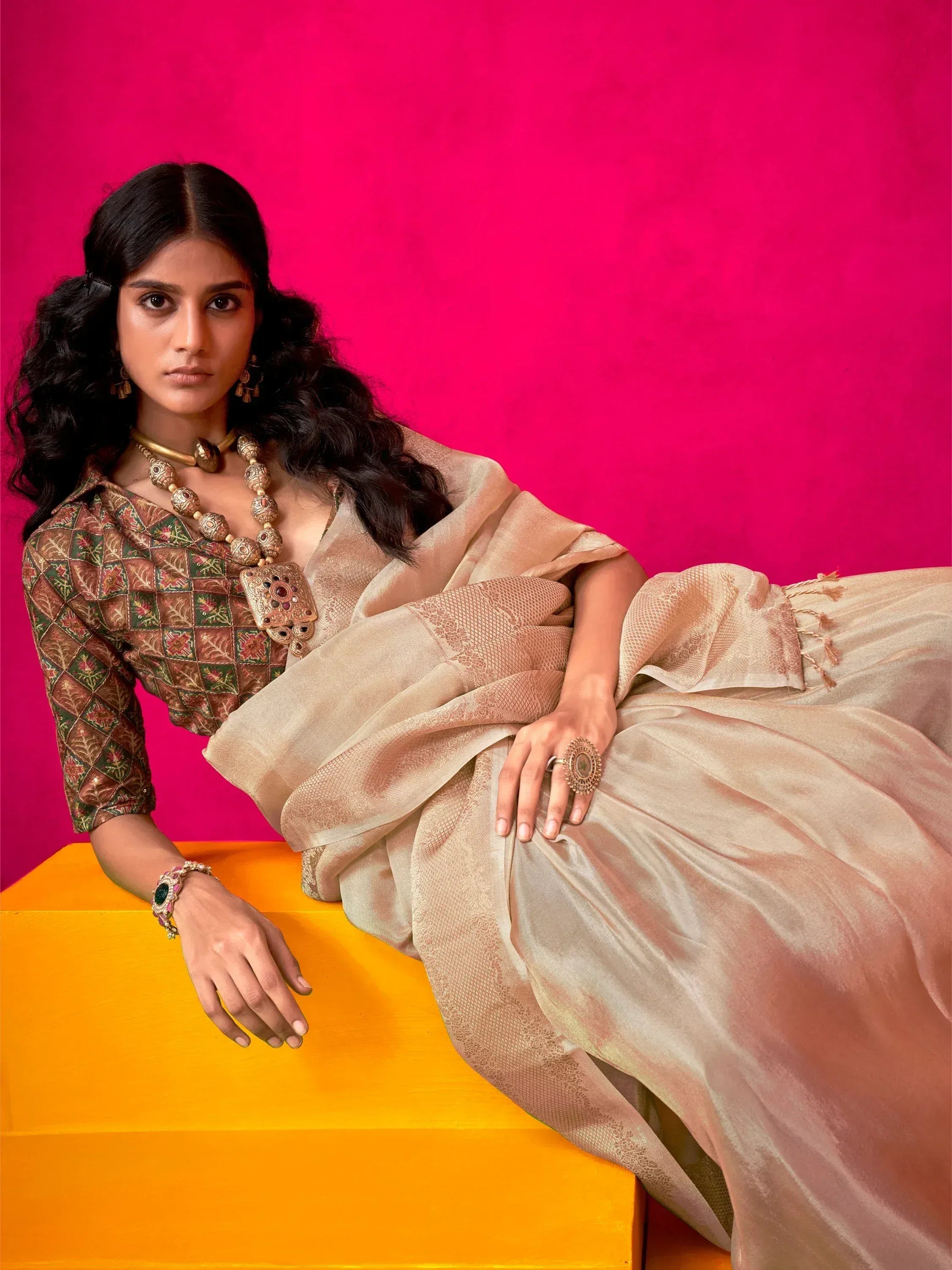 Elegant woman in designer lehenga choli with intricate embroidery and gold jewelry against vibrant pink background