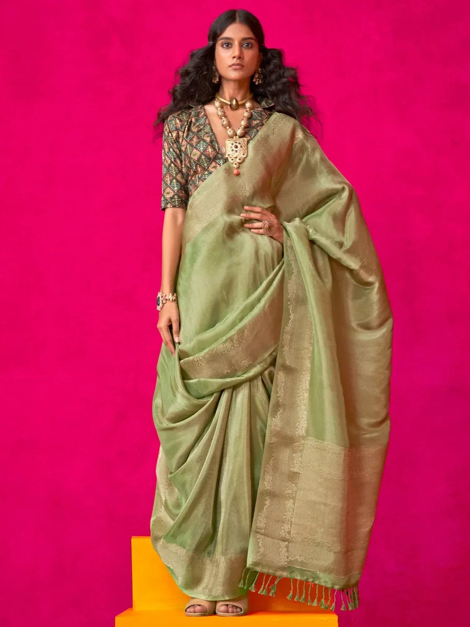 Olive green silk saree with gold border and tassels, paired with printed blouse and traditional jewelry