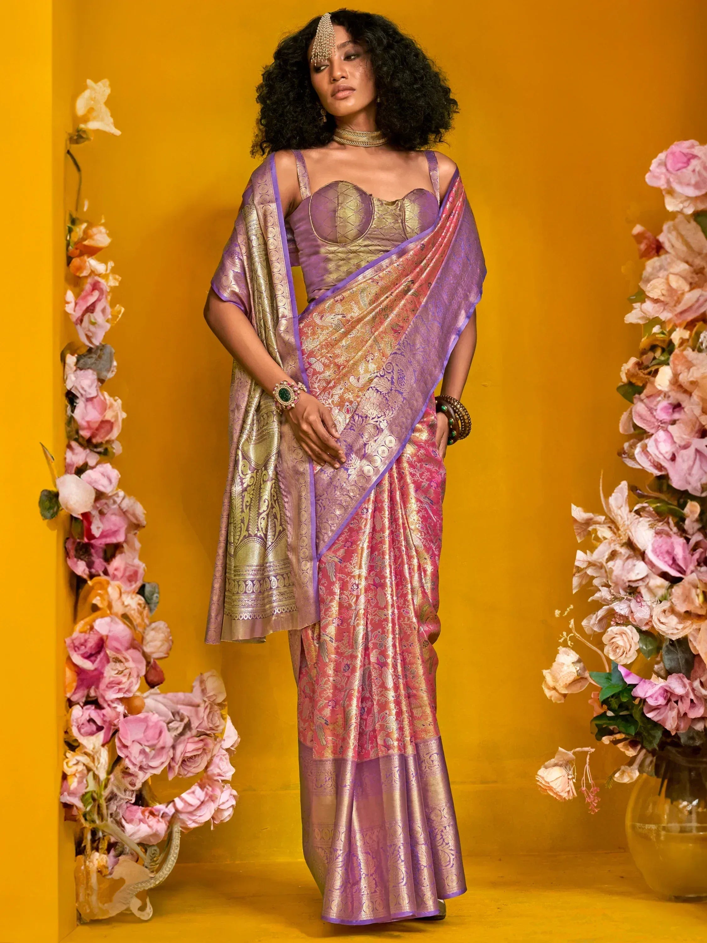 Elegant purple and pink designer saree with gold embroidery, styled with floral backdrop