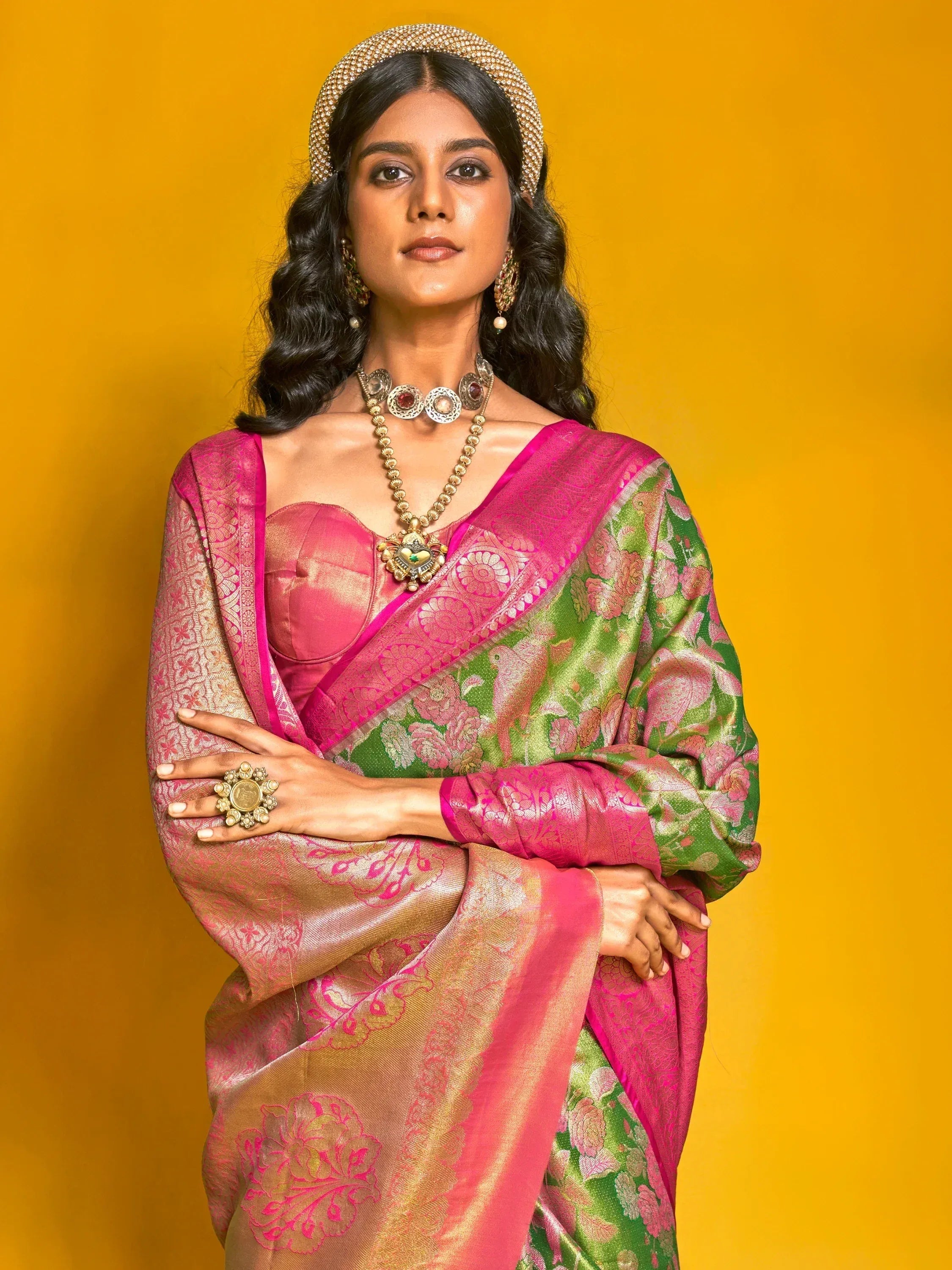 Elegant woman in vibrant pink and green floral saree with traditional jewelry against yellow backdrop