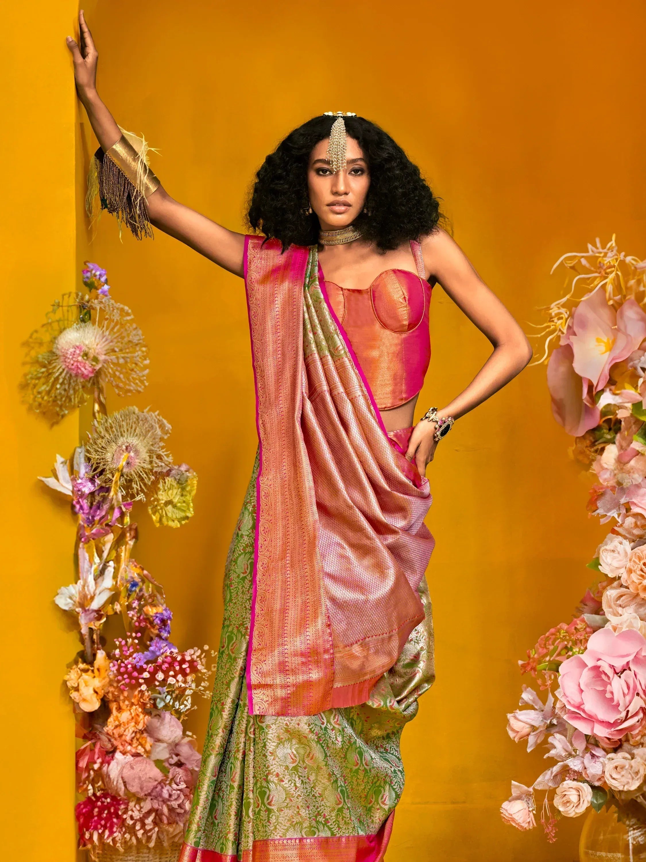 Elegant woman in vibrant pink and green saree with gold embroidery, styled with floral decor