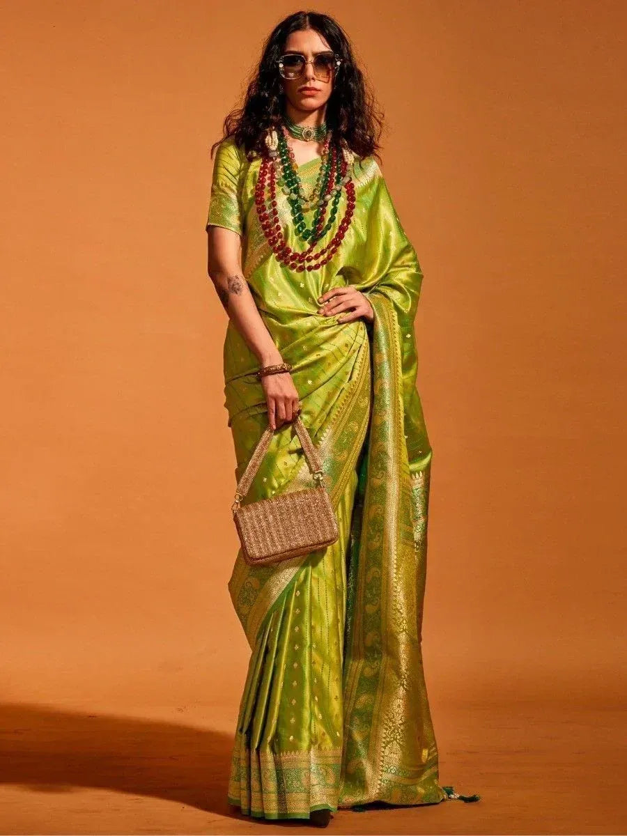 Woman in vibrant green silk saree with gold border, styled with layered necklaces and woven handbag