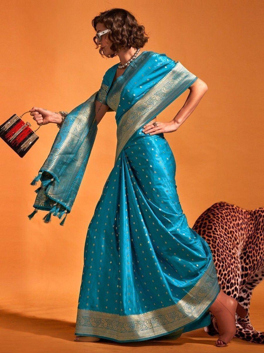Turquoise designer saree with gold motifs and border, paired with statement clutch and sunglasses