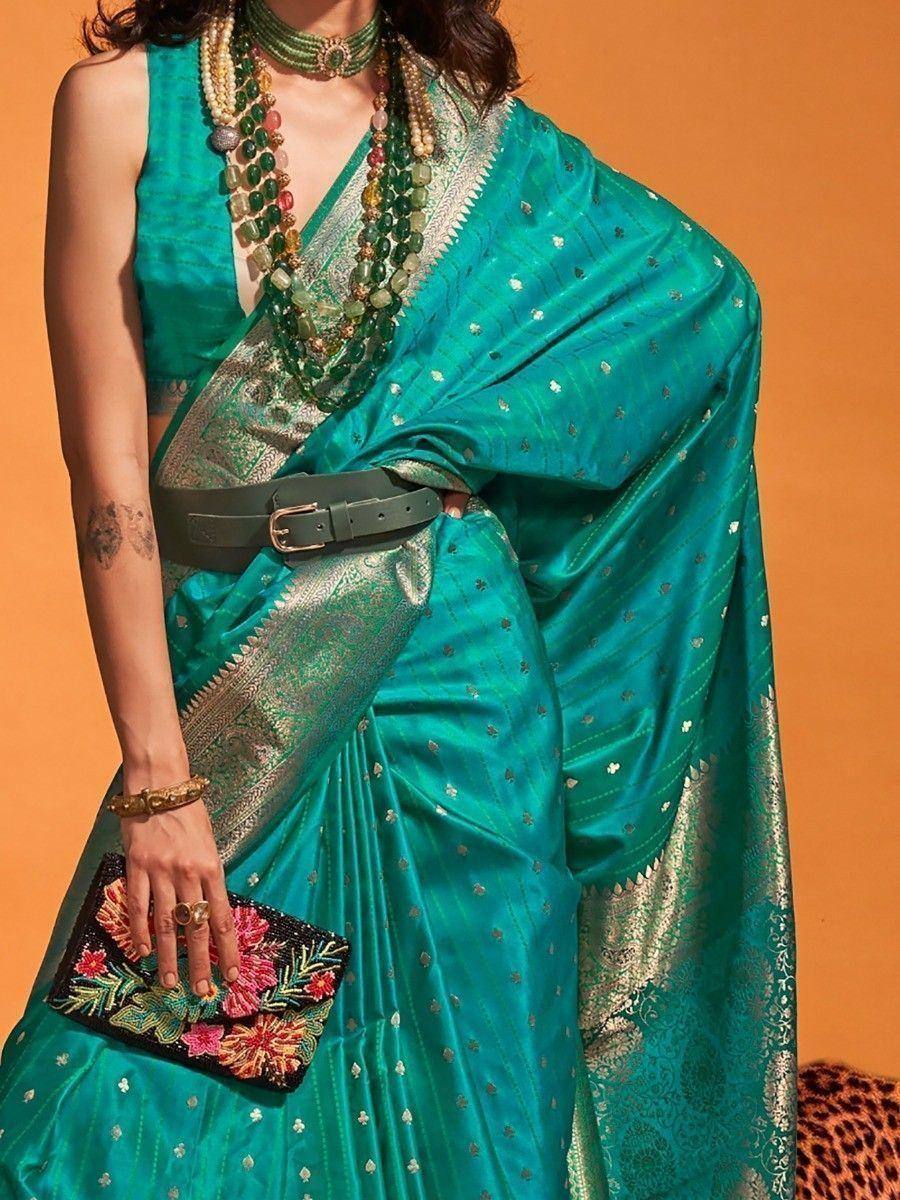 Teal silk saree with gold motifs, green blouse, statement jewelry, and floral clutch for ethnic wear