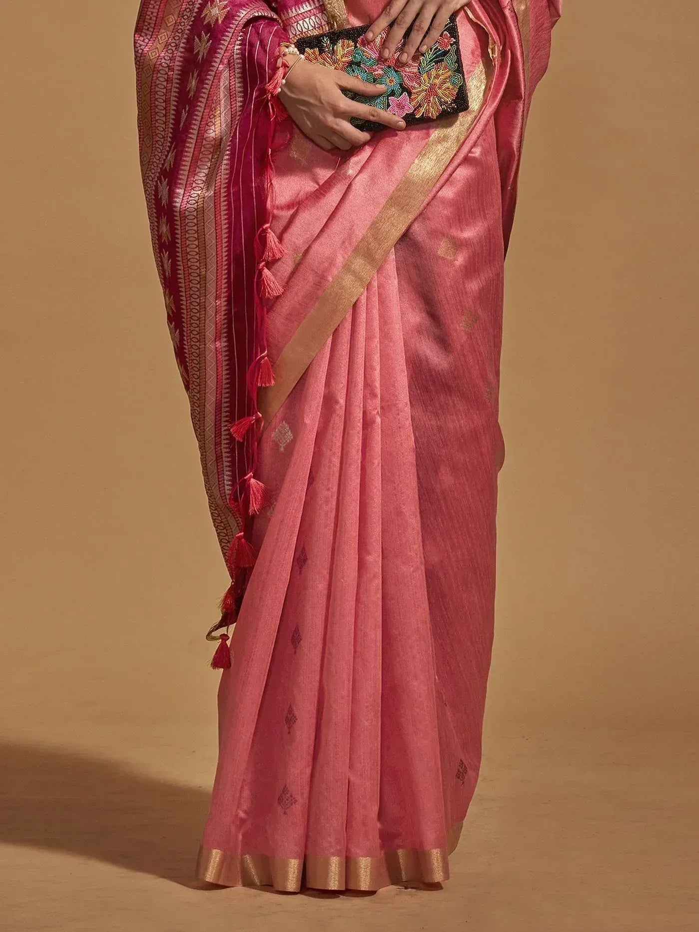 Pink silk saree with gold border and tassel pallu, paired with floral clutch for ethnic wear