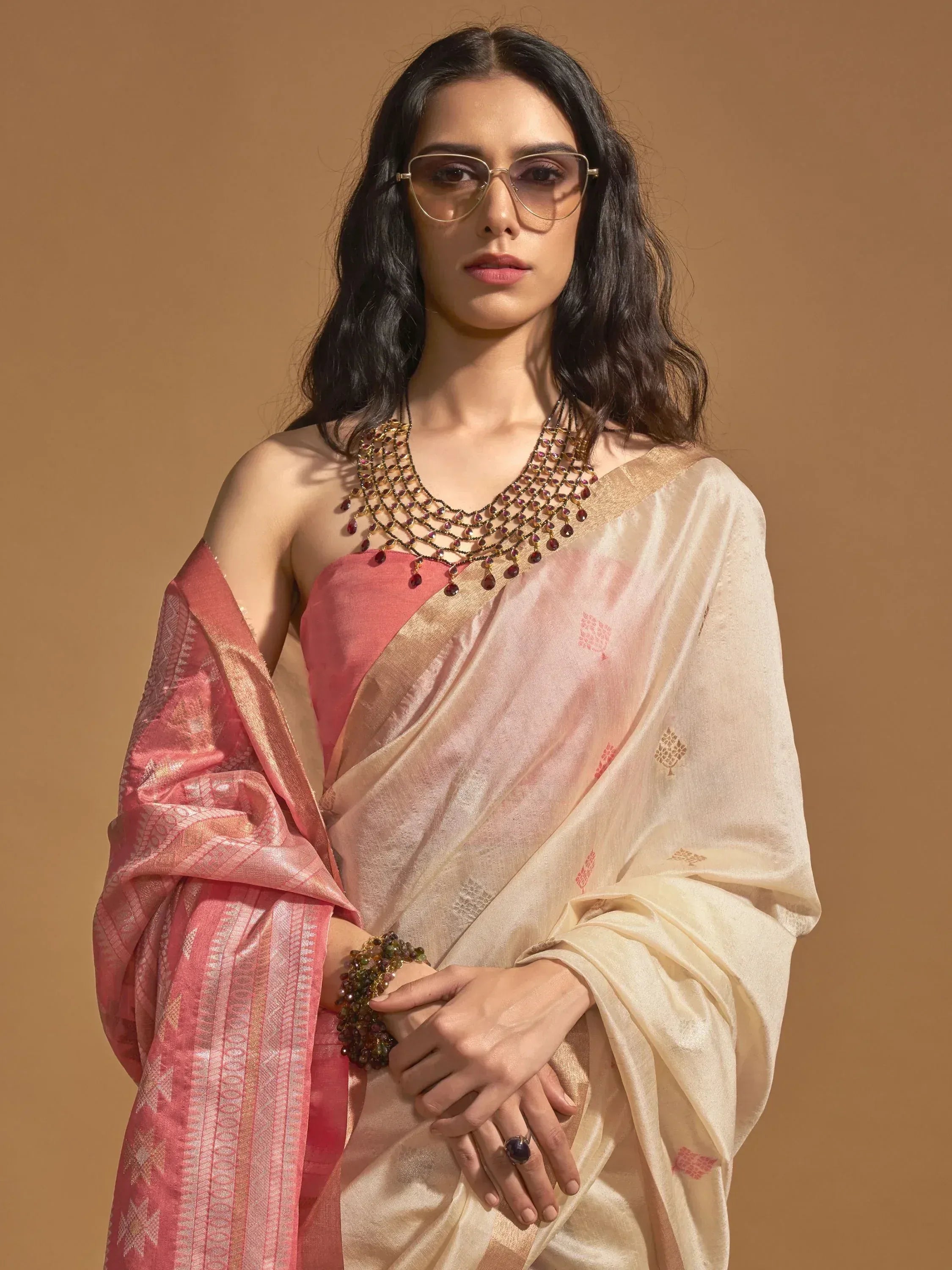Elegant woman in pink and cream designer saree with gold embroidery, paired with statement jewelry and sunglasses