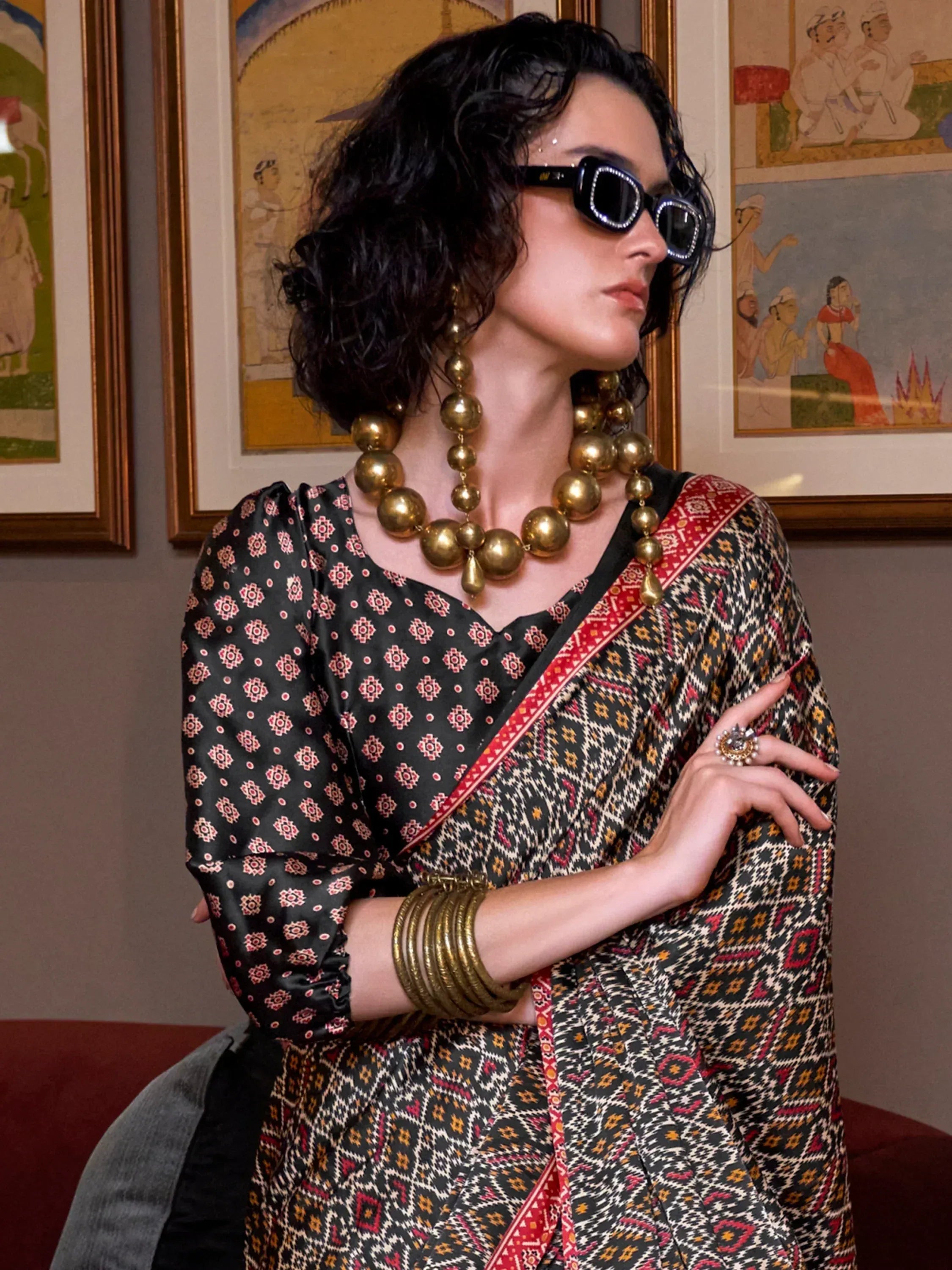 Woman in black printed ethnic saree with gold jewelry and sunglasses, styled for modern Indian fashion