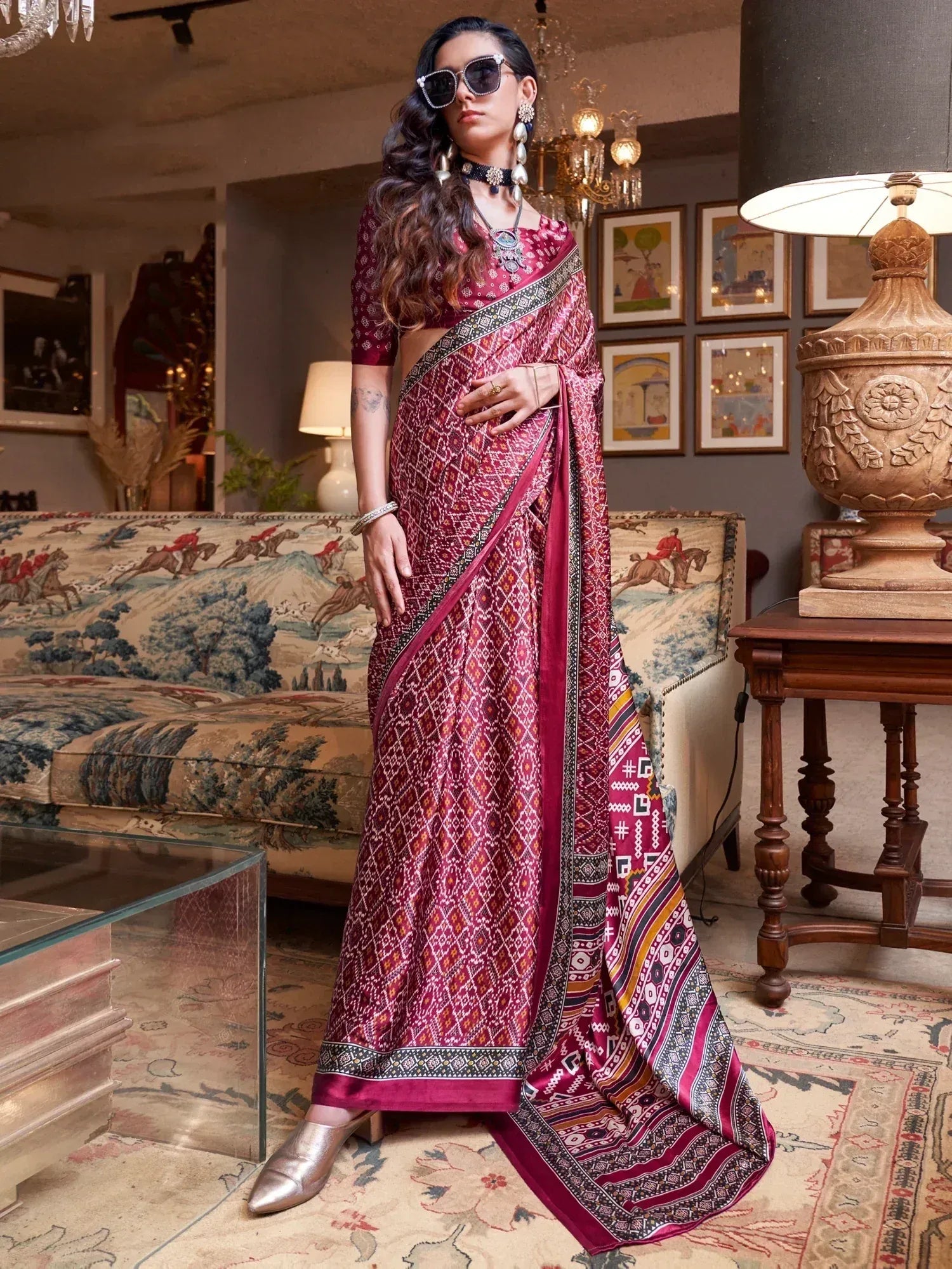 Woman in maroon printed saree with ethnic jewelry, stylish sunglasses, and metallic heels for festive occasions