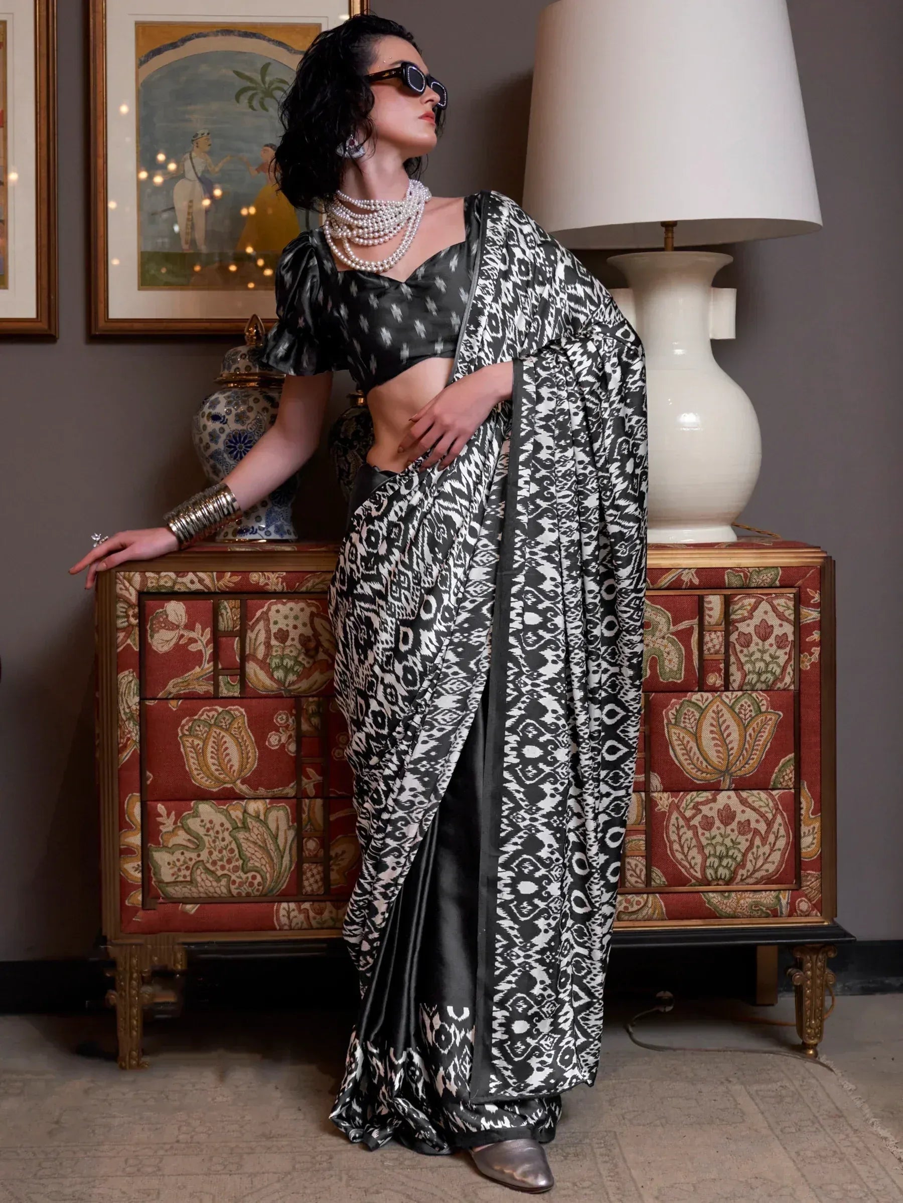 Woman in black and white ikat print saree with puff sleeve blouse, styled with pearl necklaces and sunglasses.