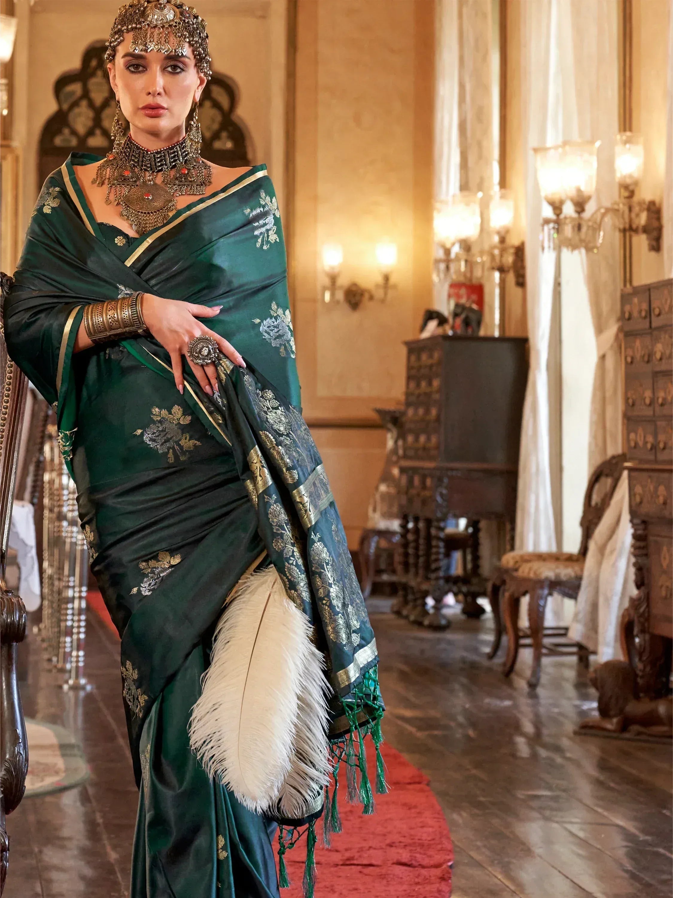 Elegant woman in emerald green designer saree with gold embroidery, traditional jewelry, and feather accessory.