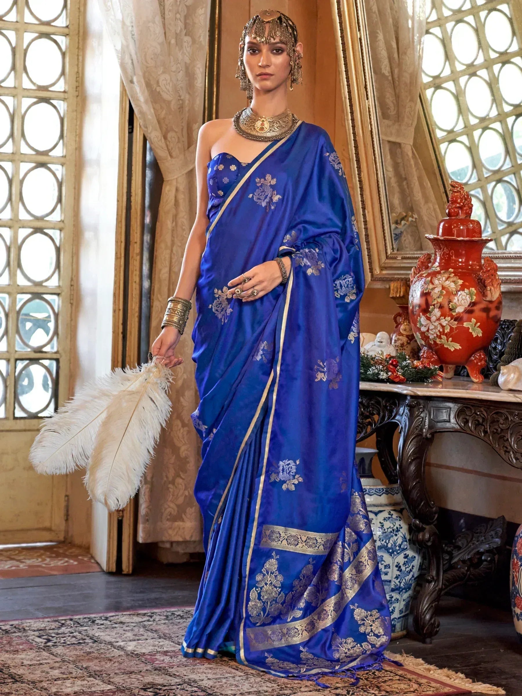 Royal blue silk saree with gold floral embroidery, paired with traditional Indian jewelry and a feather fan.