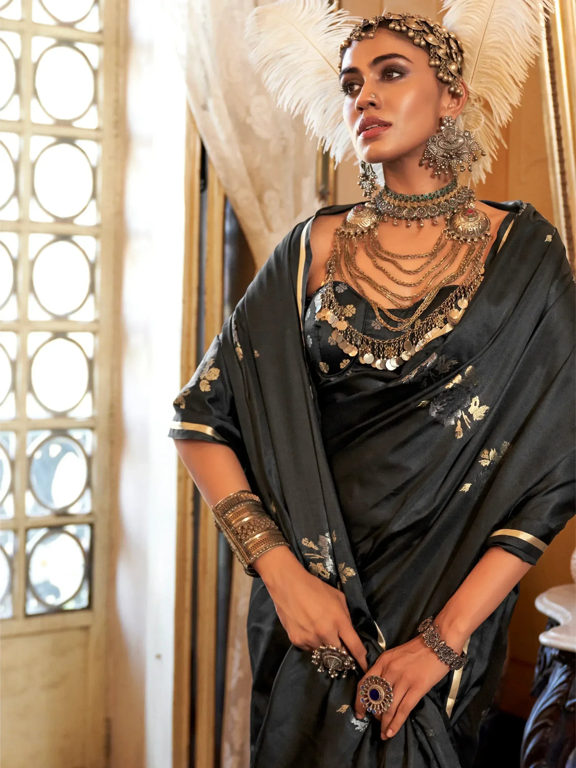 Black saree with gold embroidery, heavy ethnic jewelry, and feather headpiece for Indian festive wear