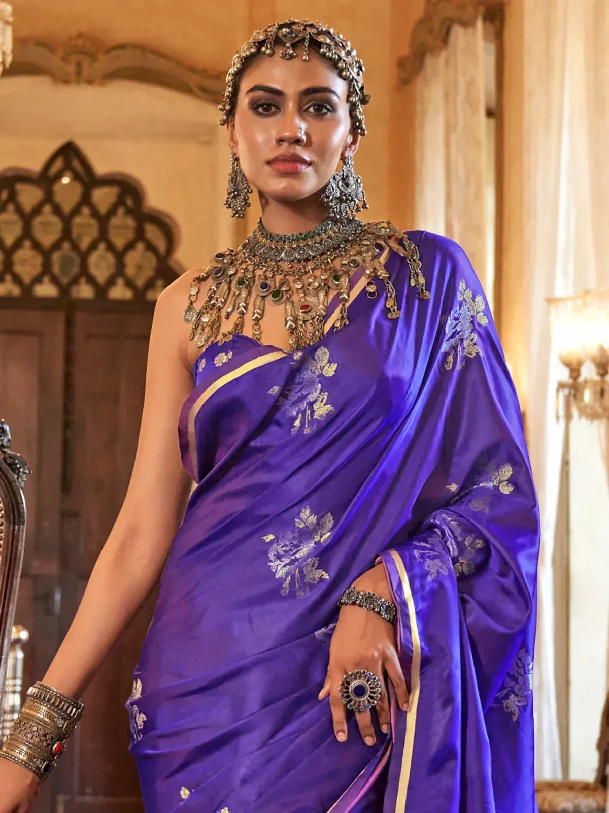 Woman in royal purple silk saree with gold floral embroidery, traditional Indian jewelry, and ethnic headpiece