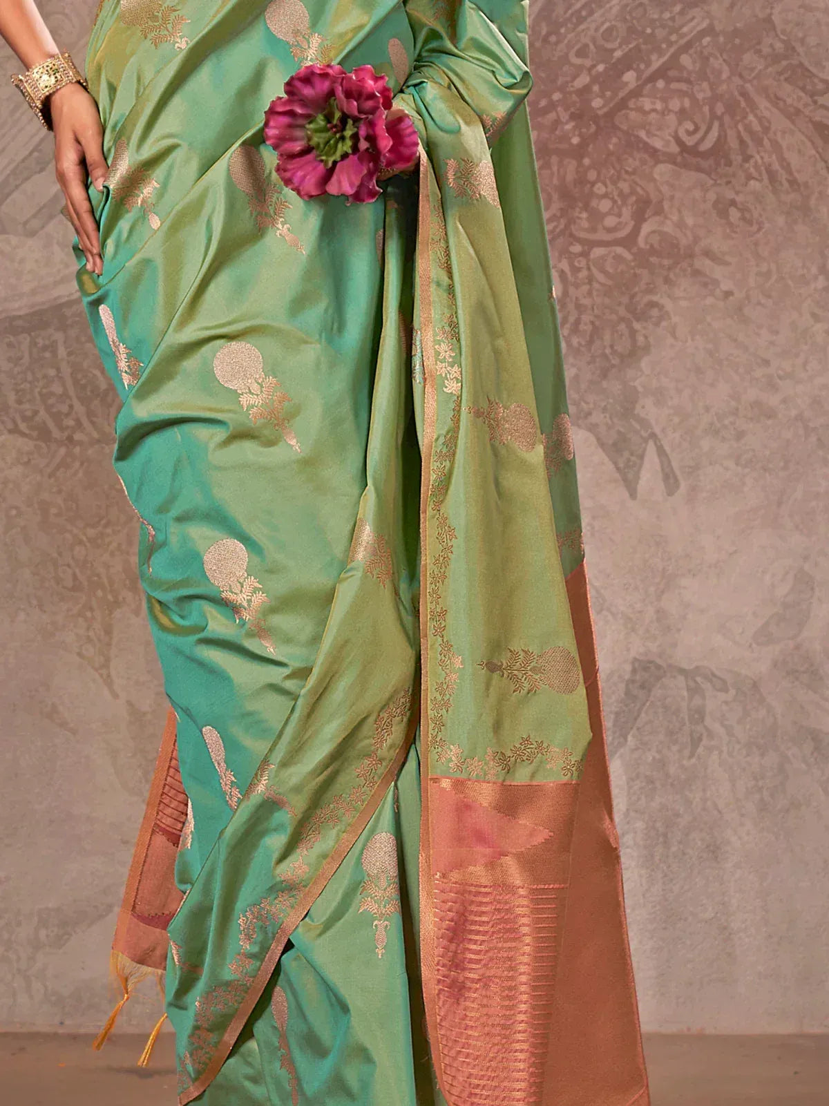 Green designer saree with gold floral motifs and pink border, styled with flowers for ethnic wear