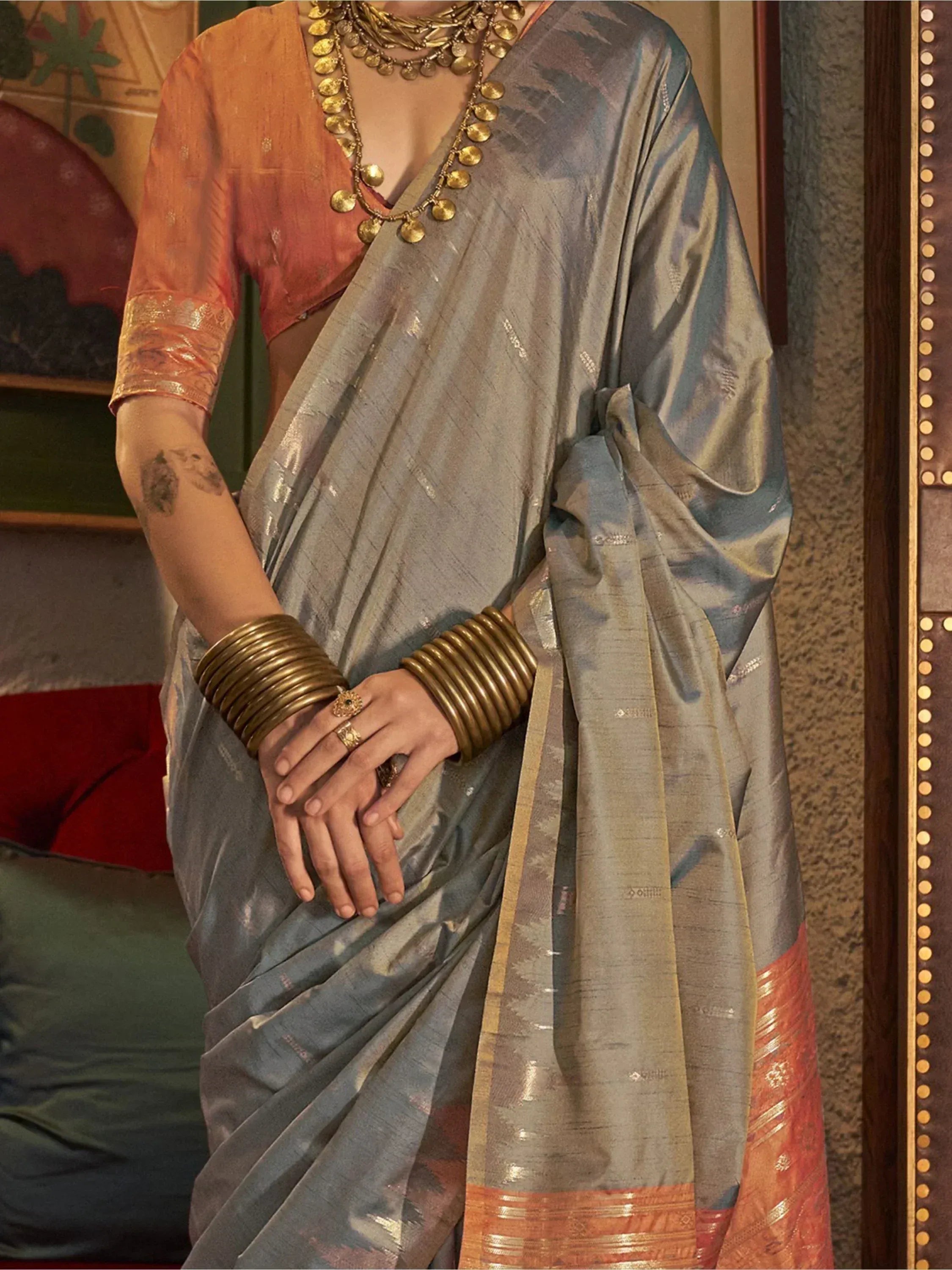 Grey silk saree with orange blouse, gold jewelry, and traditional Indian ethnic wear design