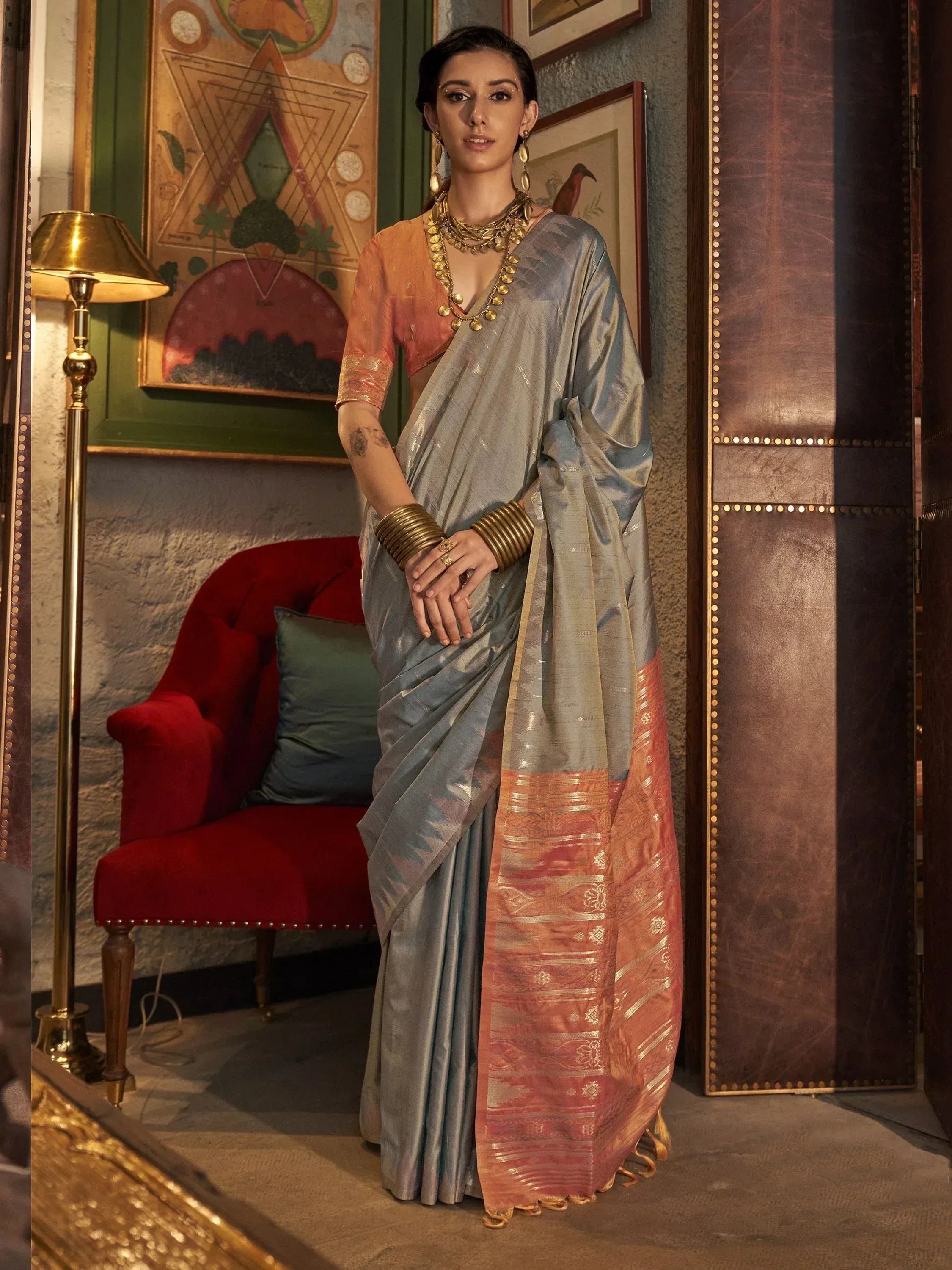 Woman in elegant grey and orange designer saree with gold jewelry, styled for ethnic occasions