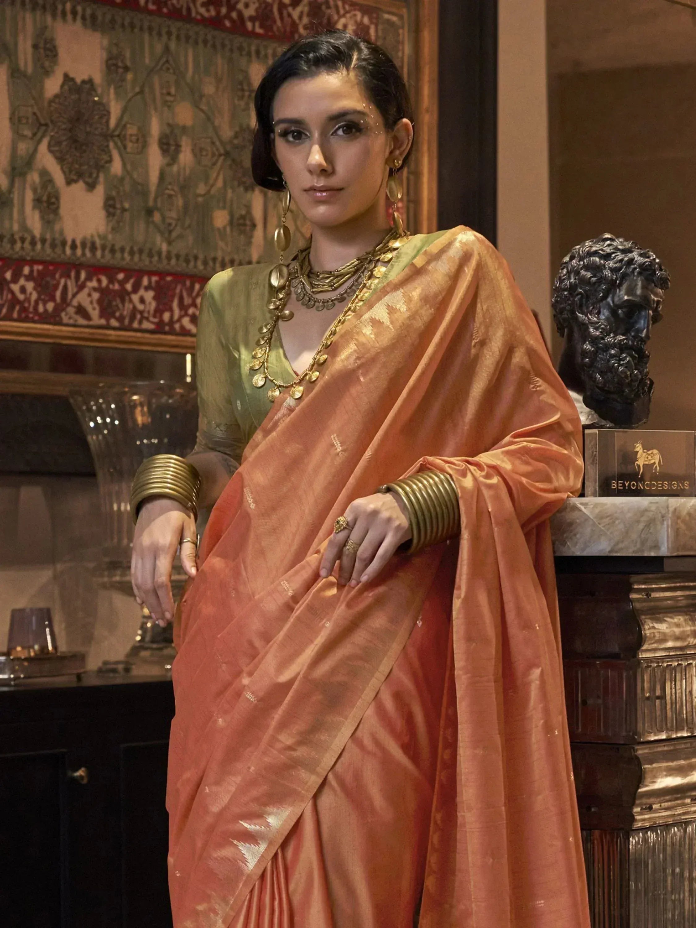 Woman in peach silk saree with gold embroidery, green blouse, and traditional Indian jewelry