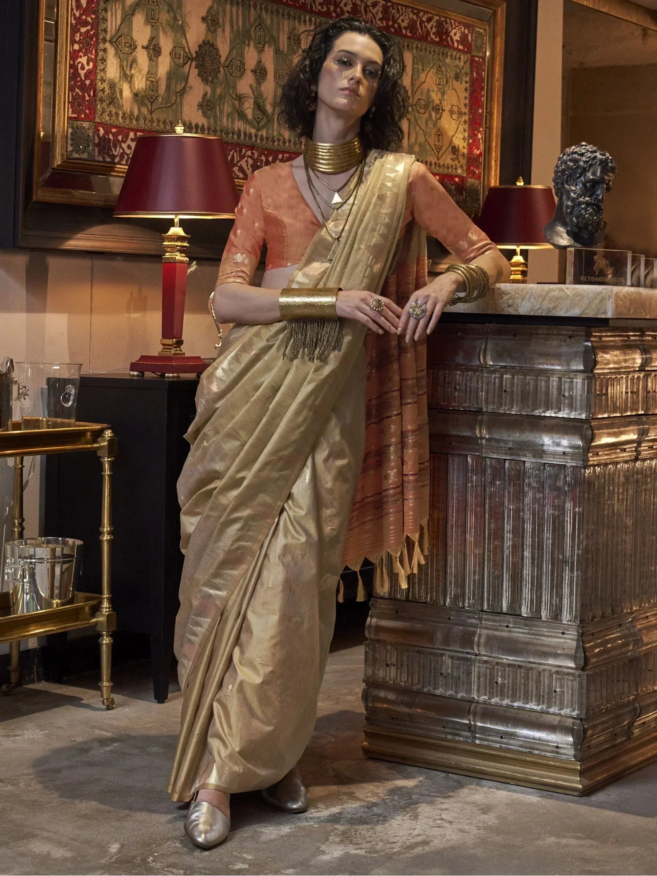 Woman in elegant gold saree with peach blouse, traditional Indian ethnic wear, styled with gold jewelry.