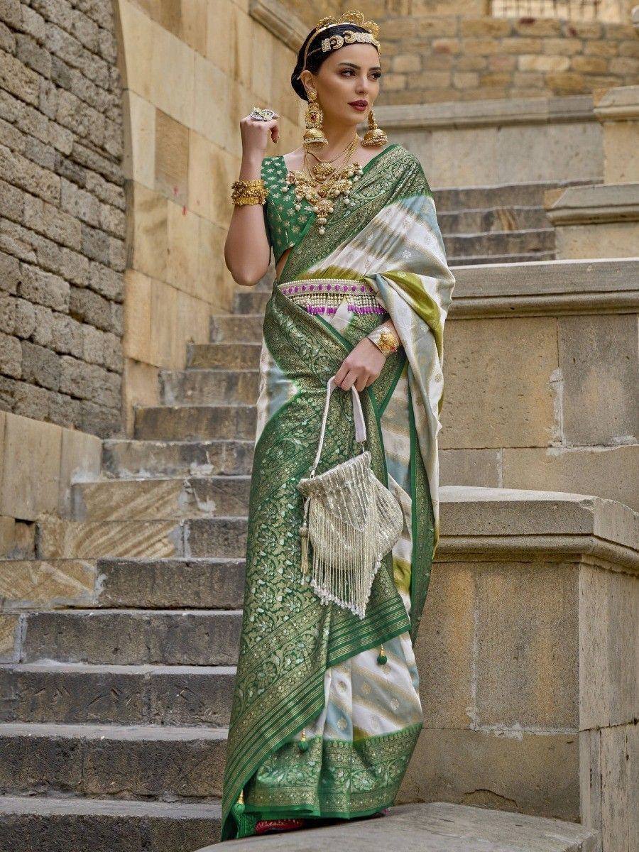 Elegant green and white designer saree with gold embroidery, paired with traditional jewelry and a fringed handbag.