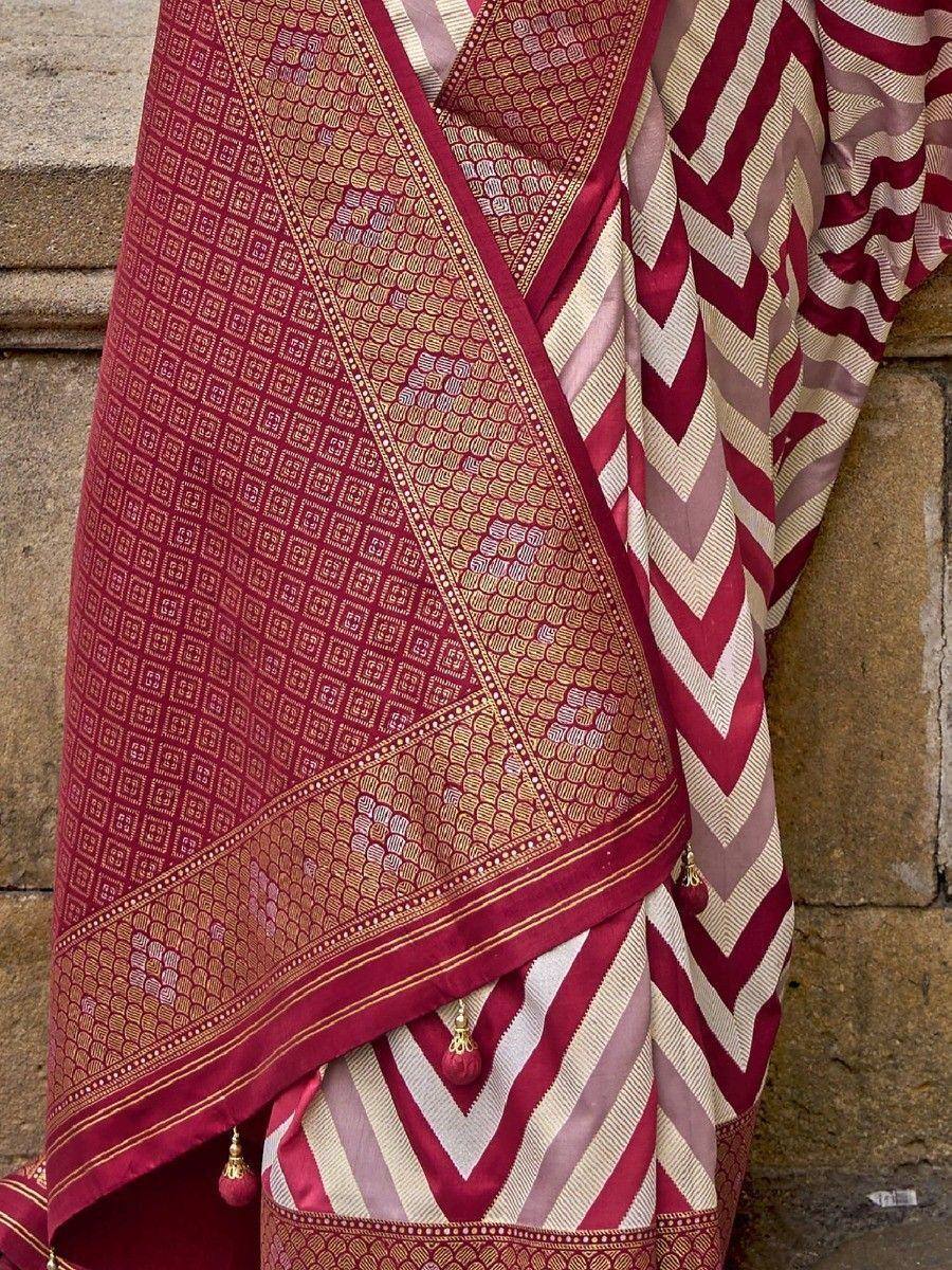 Maroon and cream ethnic saree with geometric and chevron patterns, gold detailing, tassels, draped on stone steps