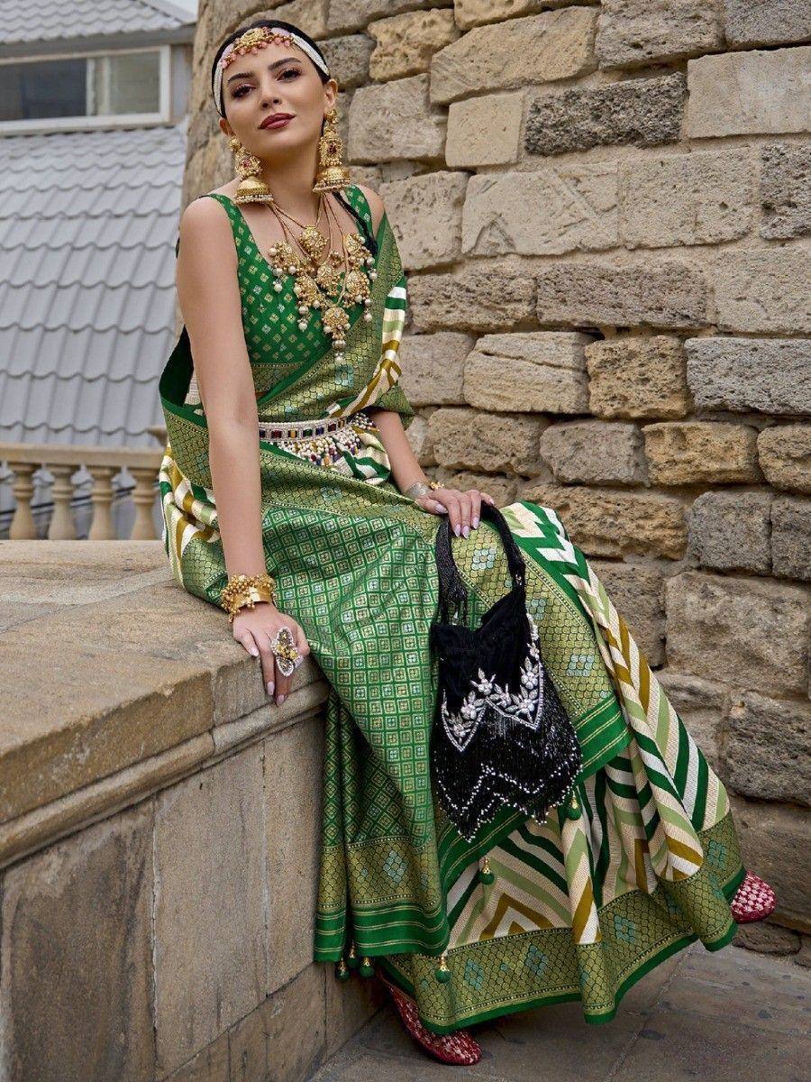 Woman in green printed lehenga choli with gold jewelry, sitting by stone wall