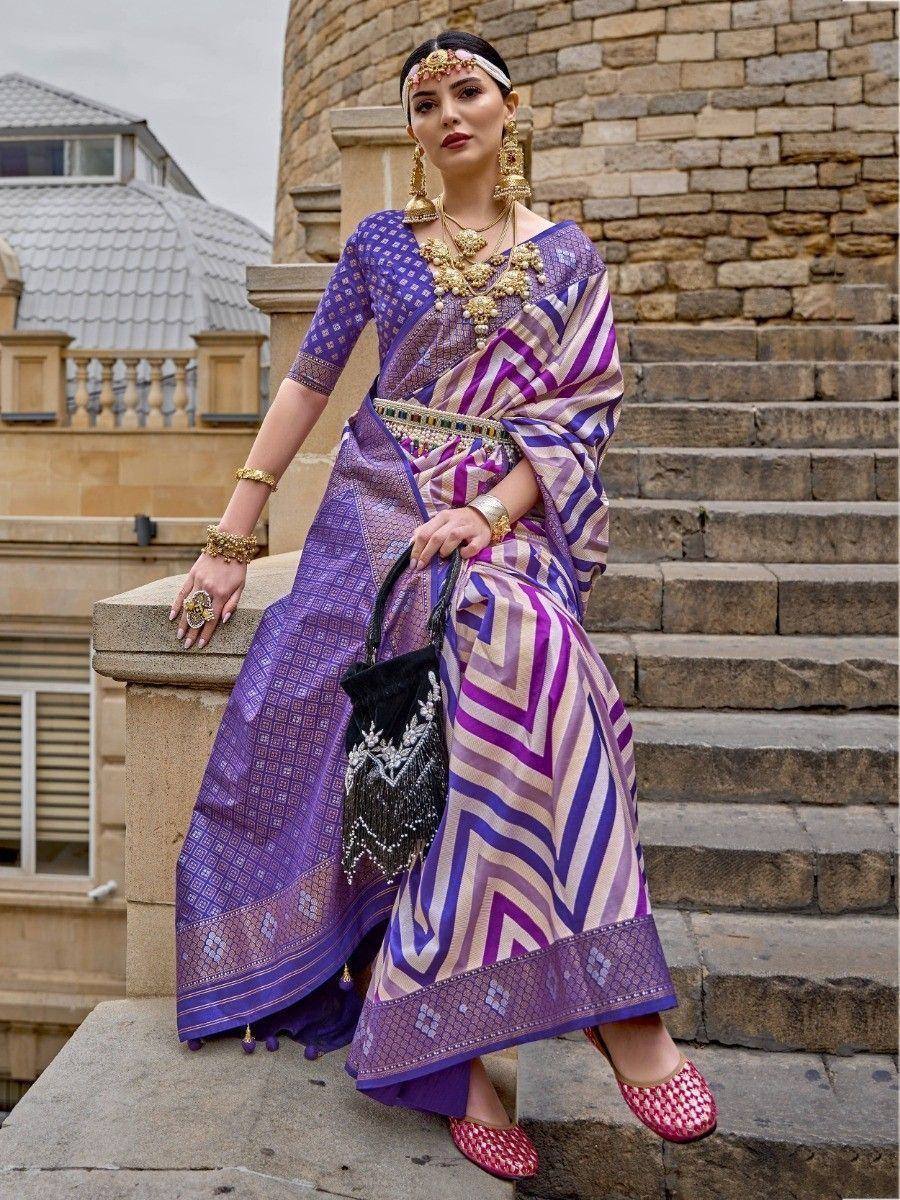 Woman in purple and pink ethnic saree with gold jewelry, standing on stone steps