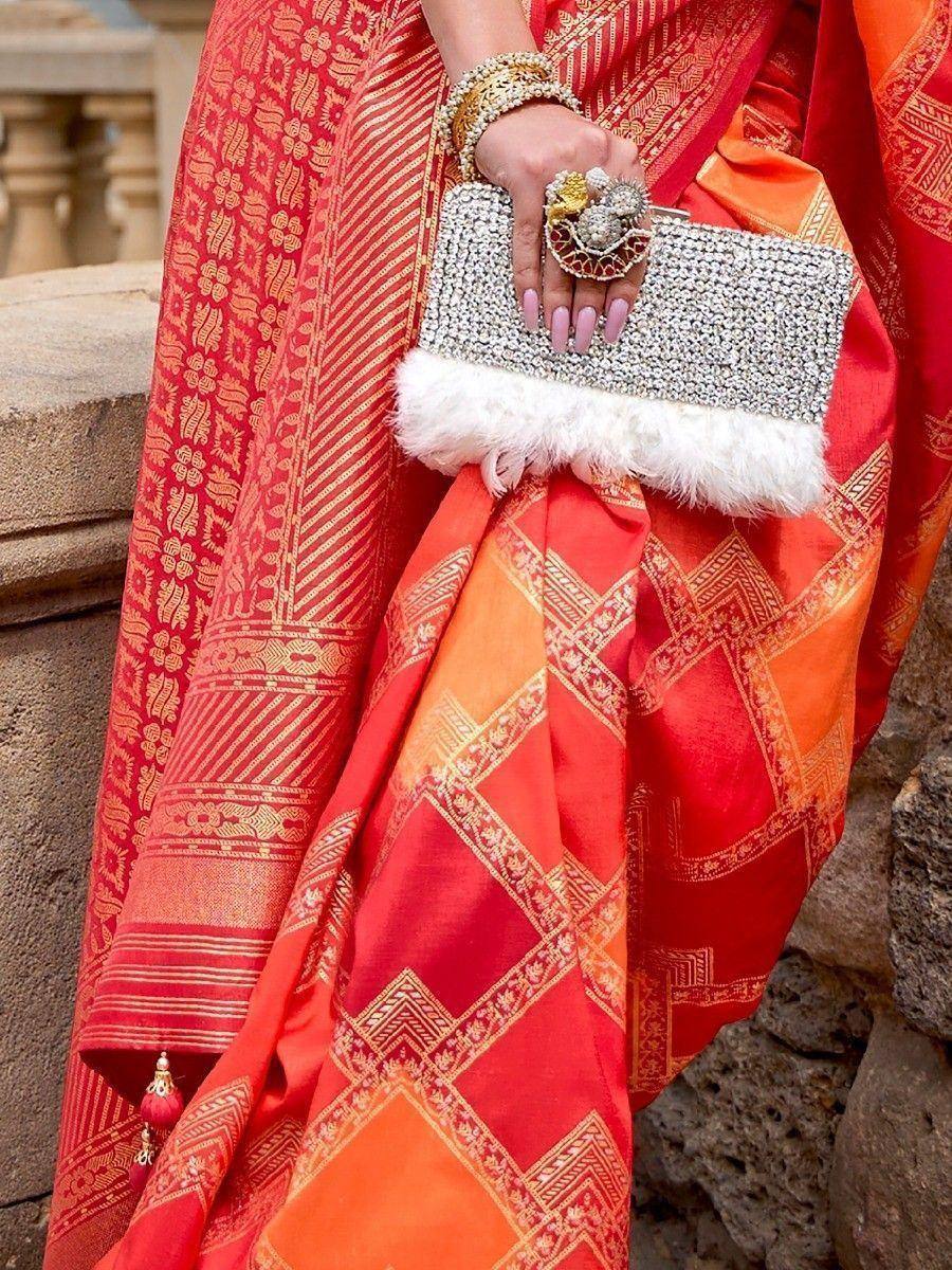 Red and orange ethnic saree with gold patterns, paired with a crystal clutch and traditional jewelry