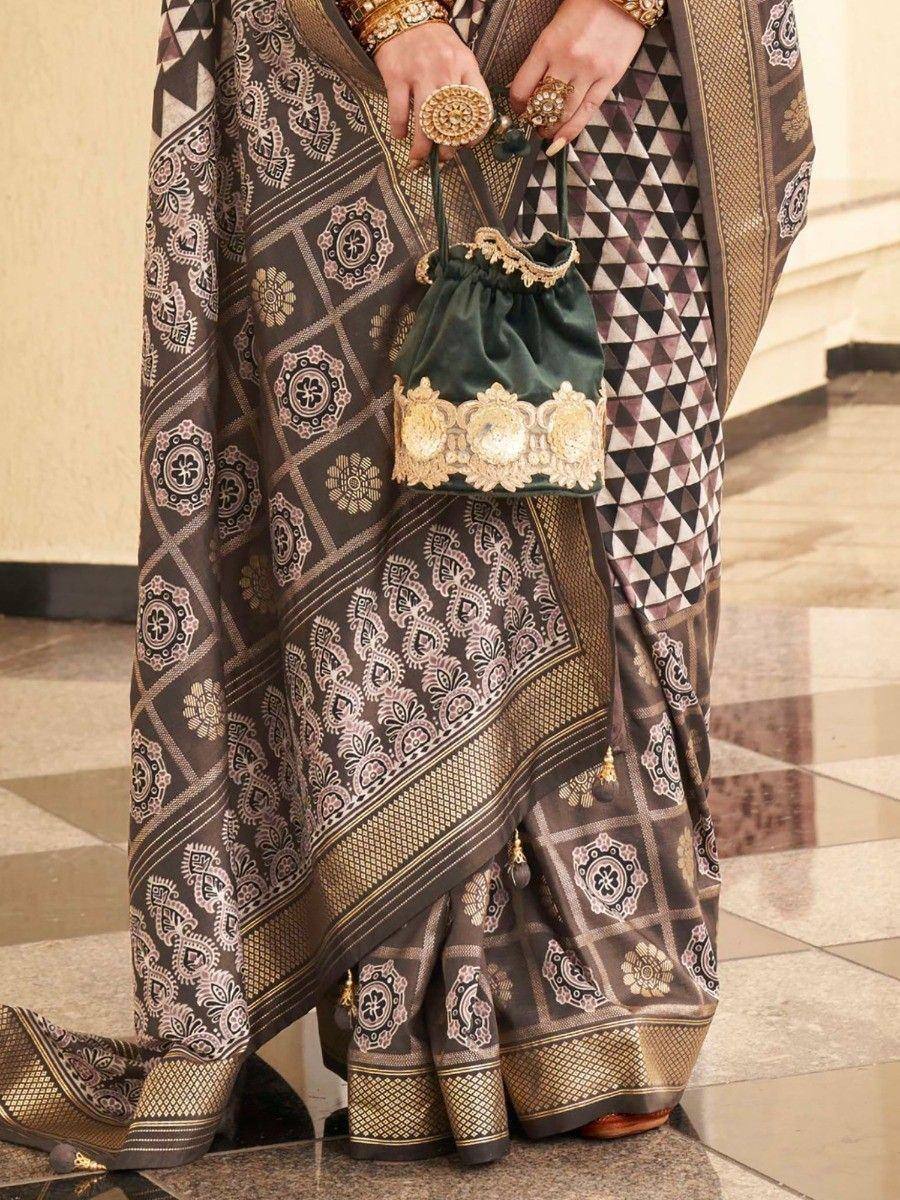 Elegant Indian saree with geometric and floral print, paired with gold jewelry and velvet potli bag