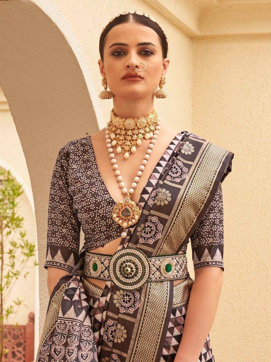 Elegant Indian ethnic saree with intricate geometric print, paired with statement gold jewelry and a decorative belt.
