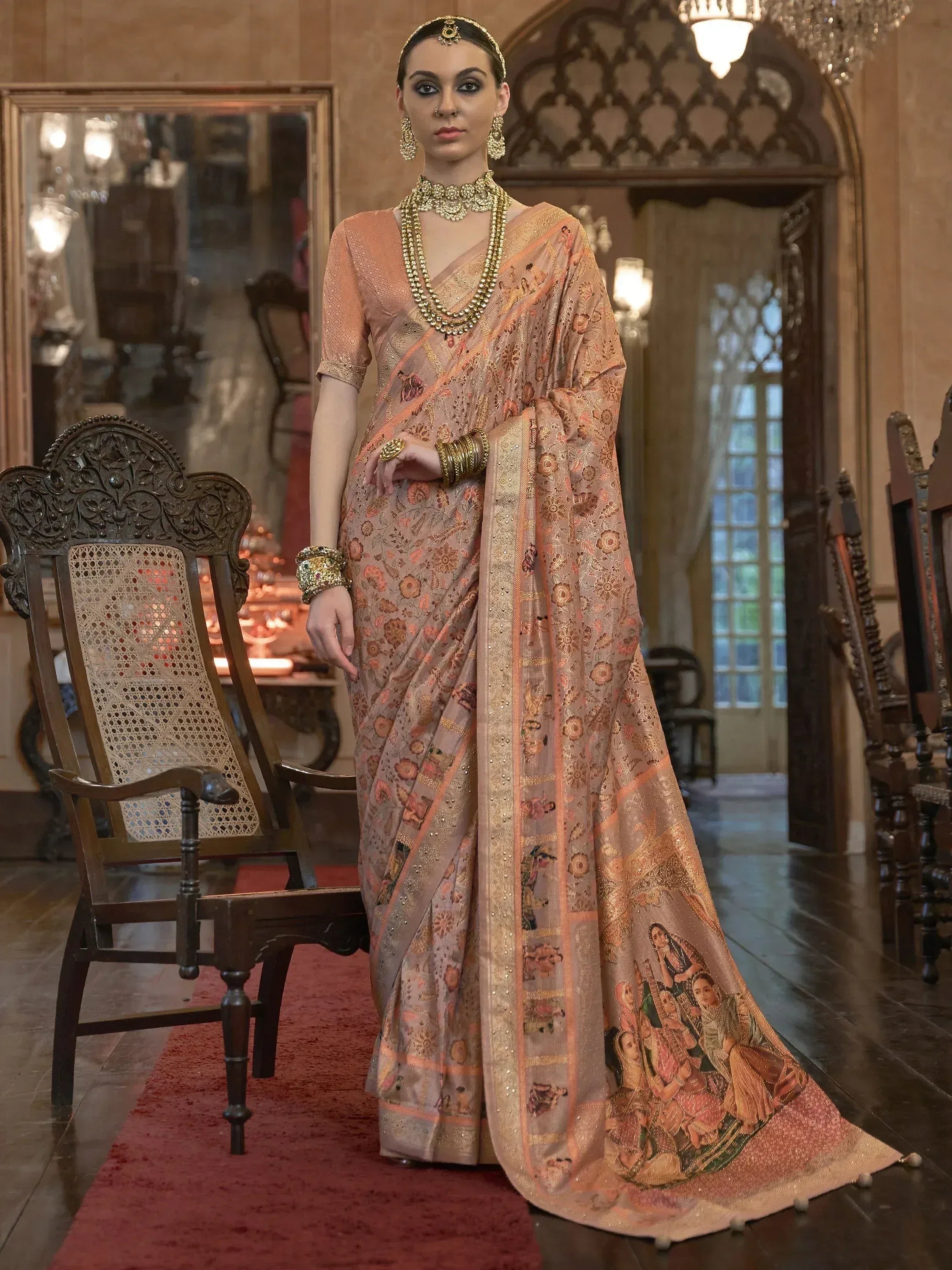 Elegant peach saree with intricate floral and figurative prints, paired with gold jewelry, perfect for Indian ethnic occasions.