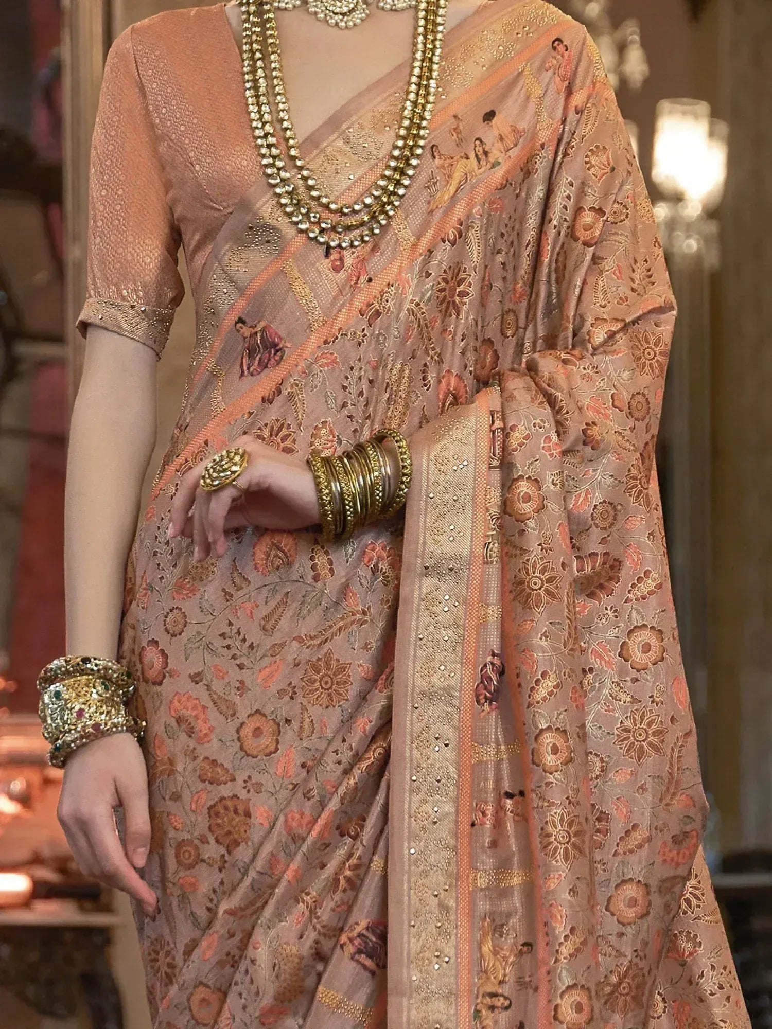 Elegant peach saree with floral and figurine print, paired with gold jewelry for Indian ethnic wear