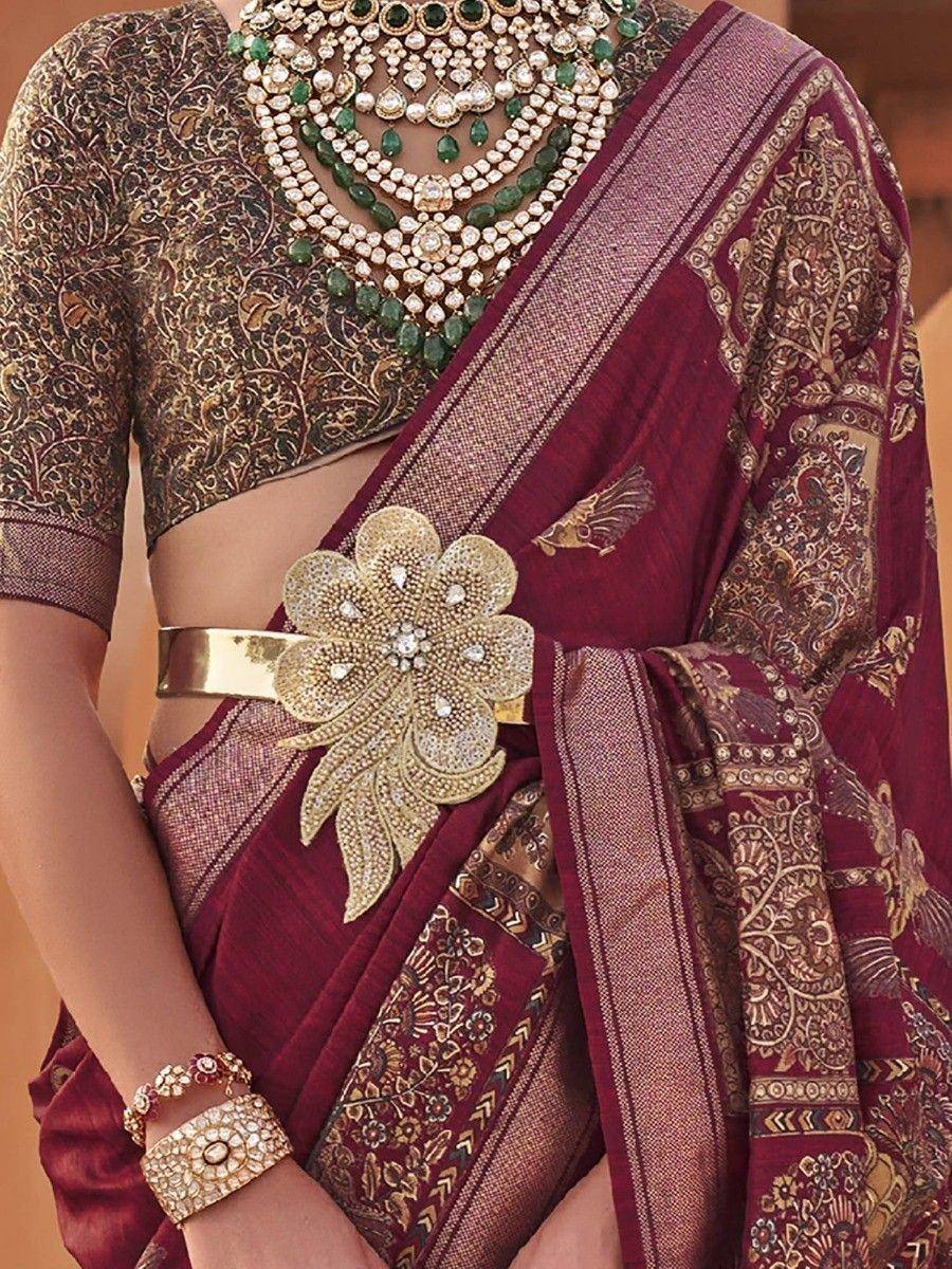 Maroon designer saree with gold embroidery, floral belt, and emerald jewelry for Indian ethnic wear