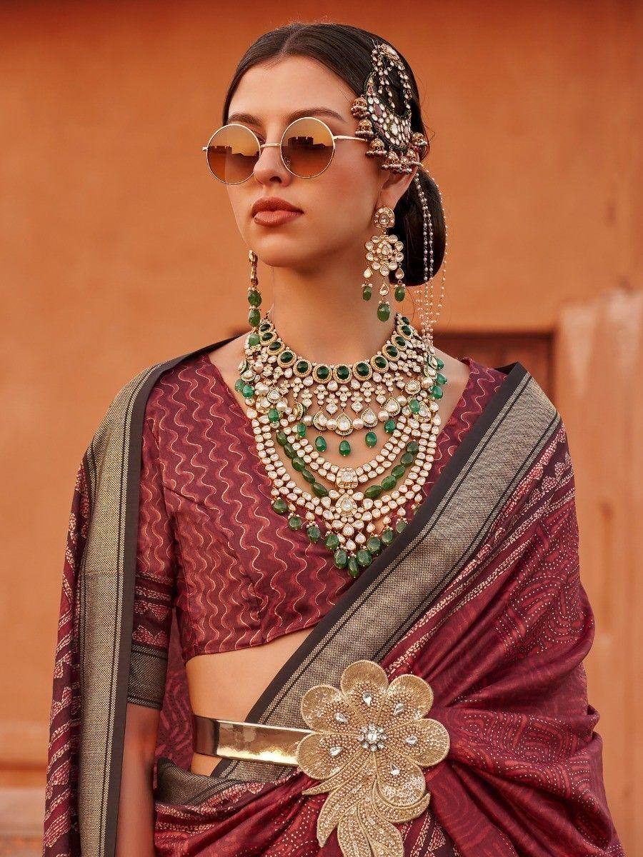 Woman in maroon ethnic saree with green jewelry and floral belt, styled for Indian occasions