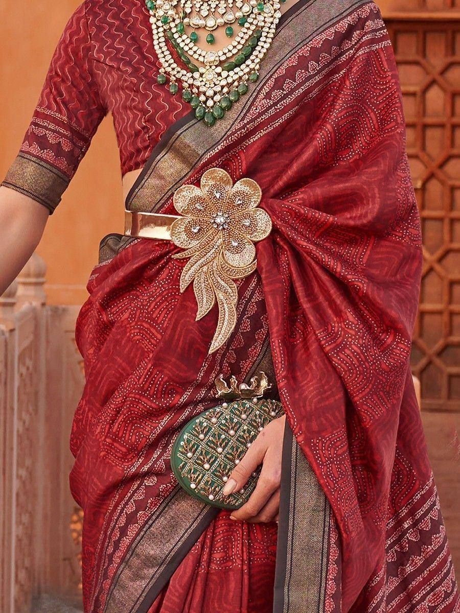 Red ethnic saree with gold floral brooch, green jewelry, and matching clutch for Indian occasions